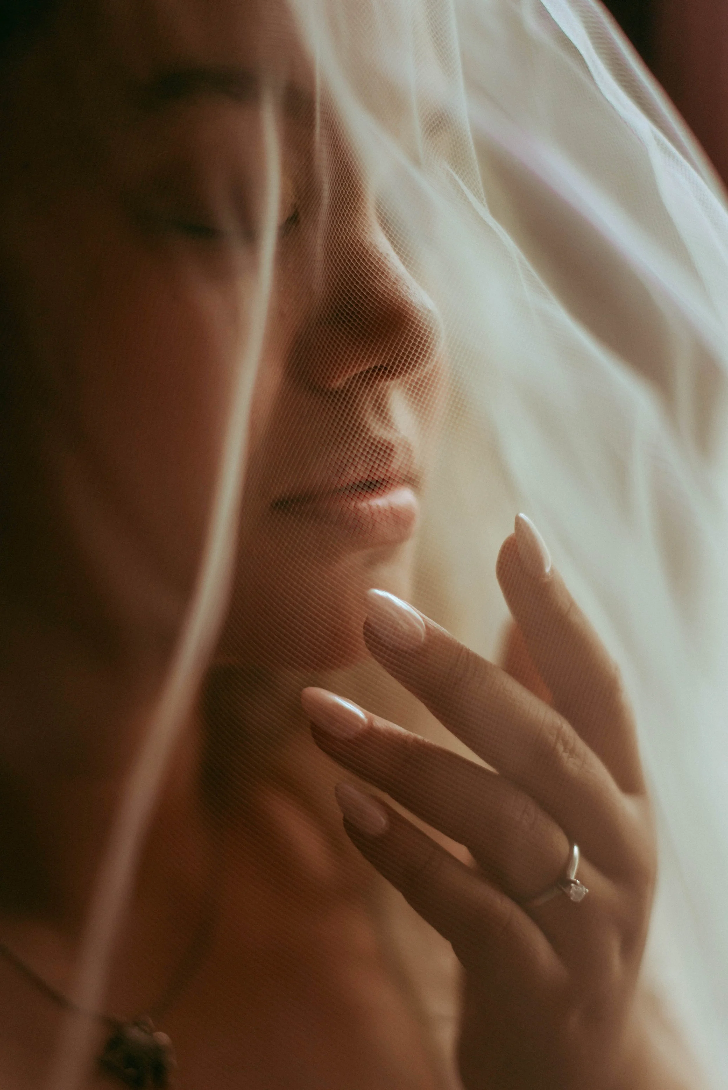 A woman behind a sheer curtain or fabric, with her hand gently touching it. The focus is on her face in profile, with closed eyes and a serene expression.