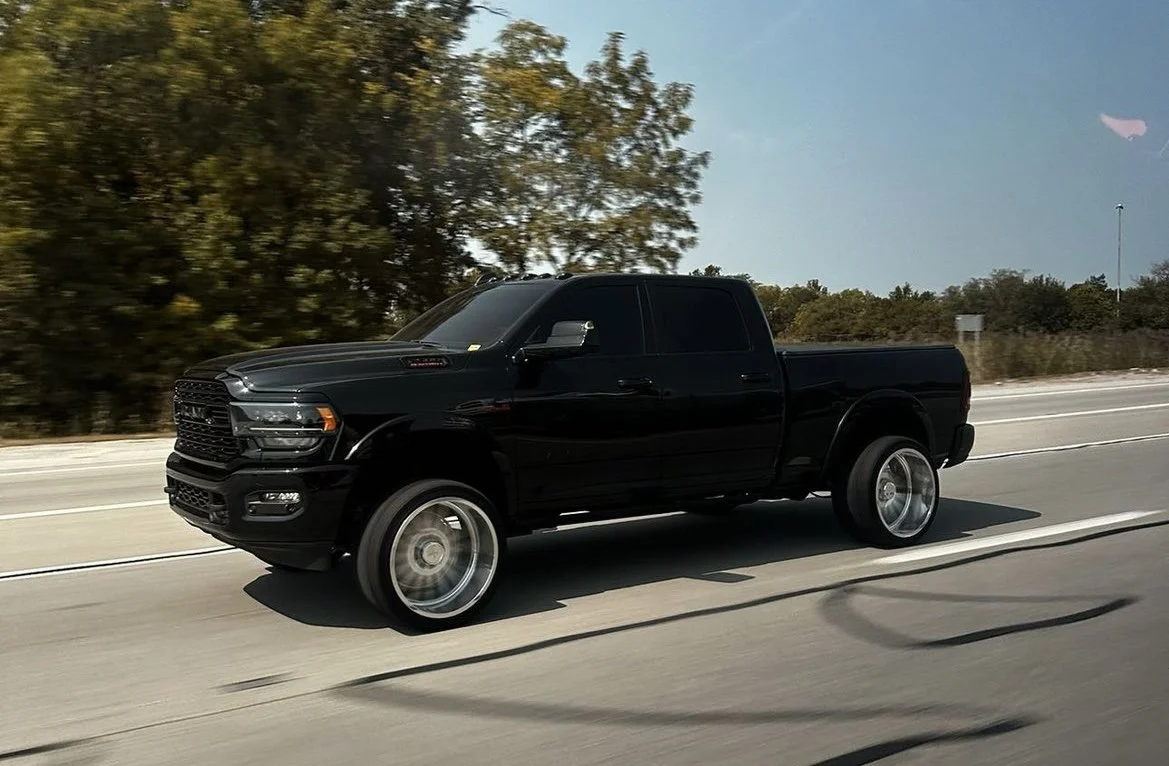 Black pickup truck driving on highway with blurred background of trees and sky