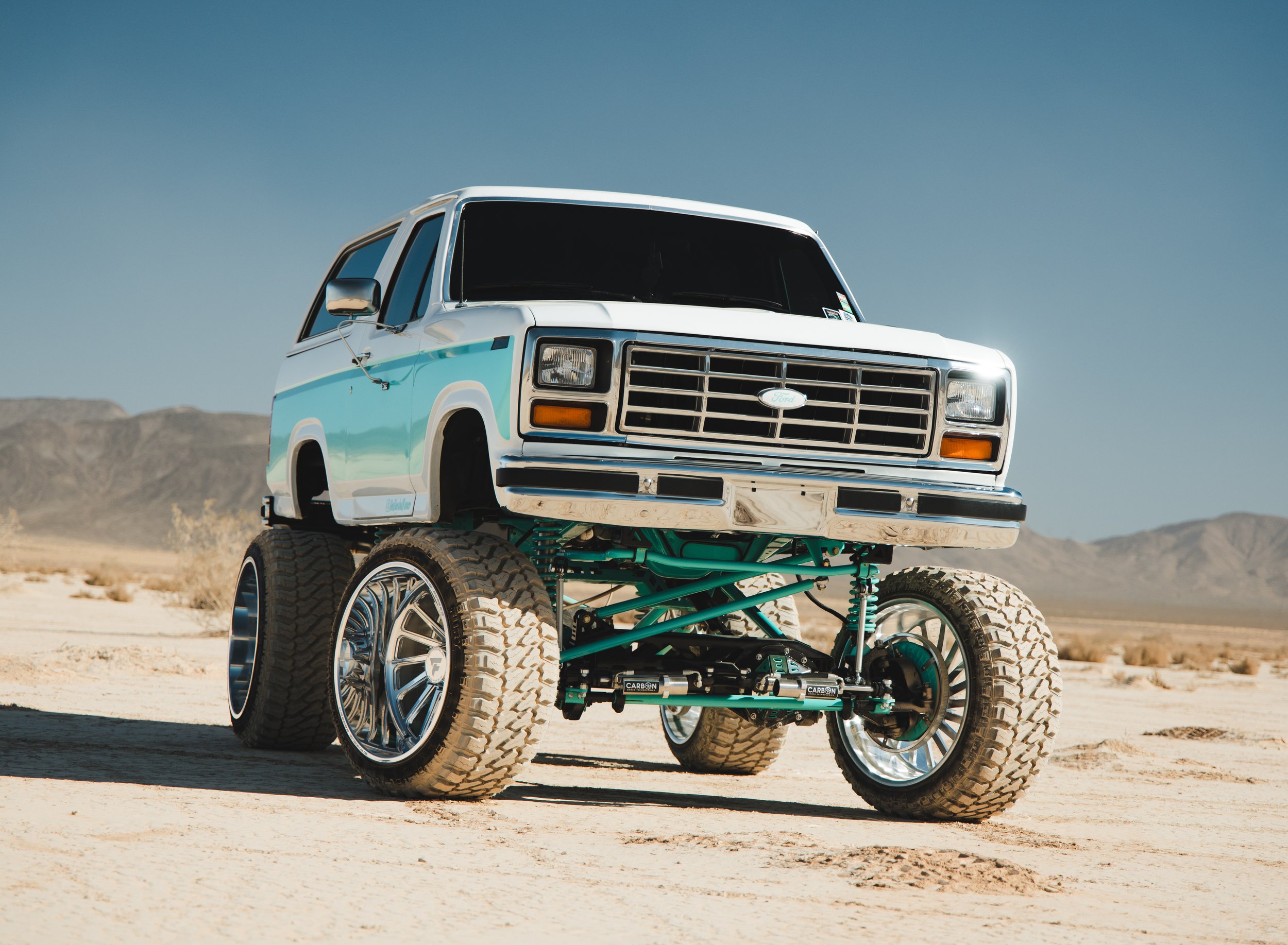 A futuristic, modified pickup truck with large off-road tires and custom suspension, parked in a desert landscape with mountains in the background and a clear blue sky.