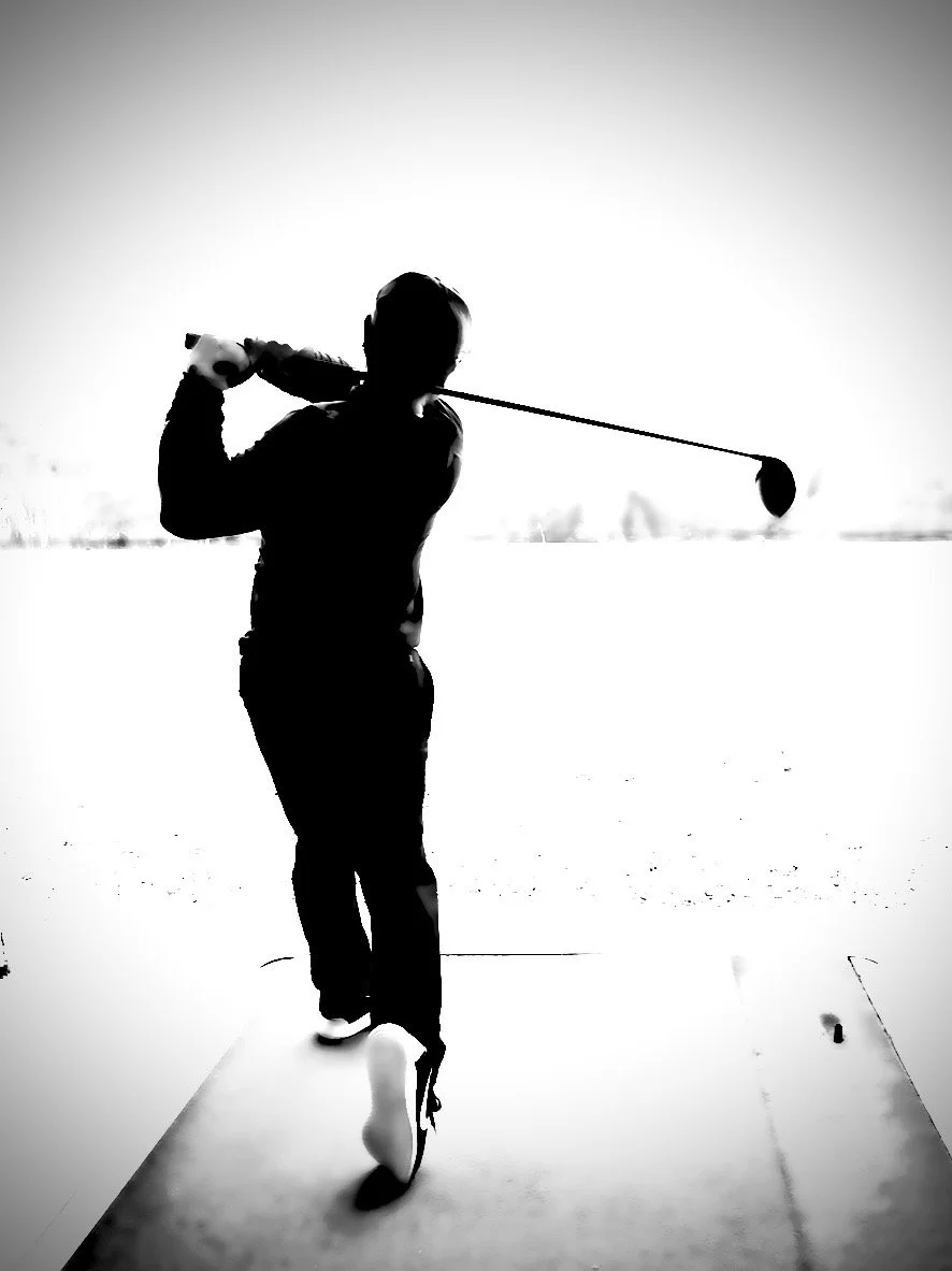 Silhouette of person swinging a golf club on an indoor driving range.