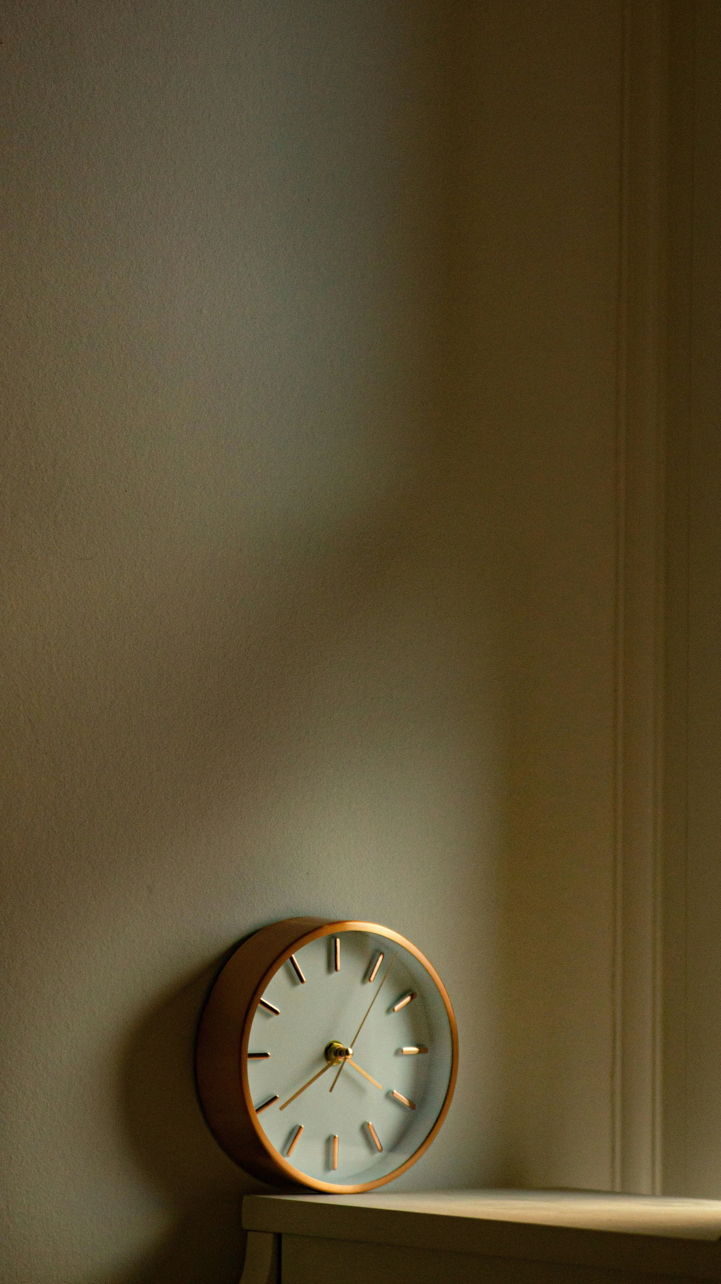 A round wall clock with a gold frame, white face, and gold hands shows the time as 4:23. The clock is mounted on a gray wall above a white piece of furniture.
