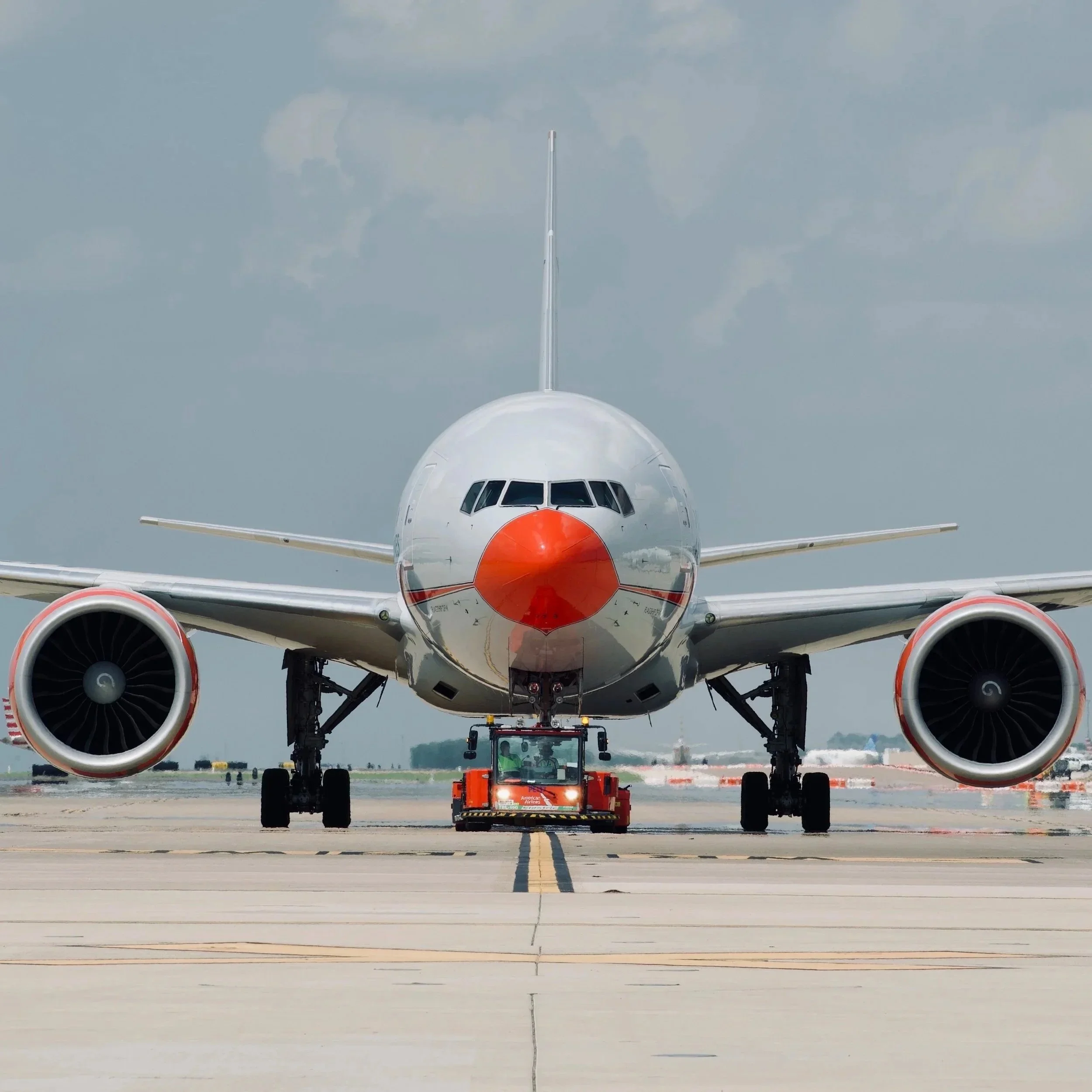 Front view of a commercial airplane on the runway, being pushed by a tow tractor, with a cloudy sky in the background.
