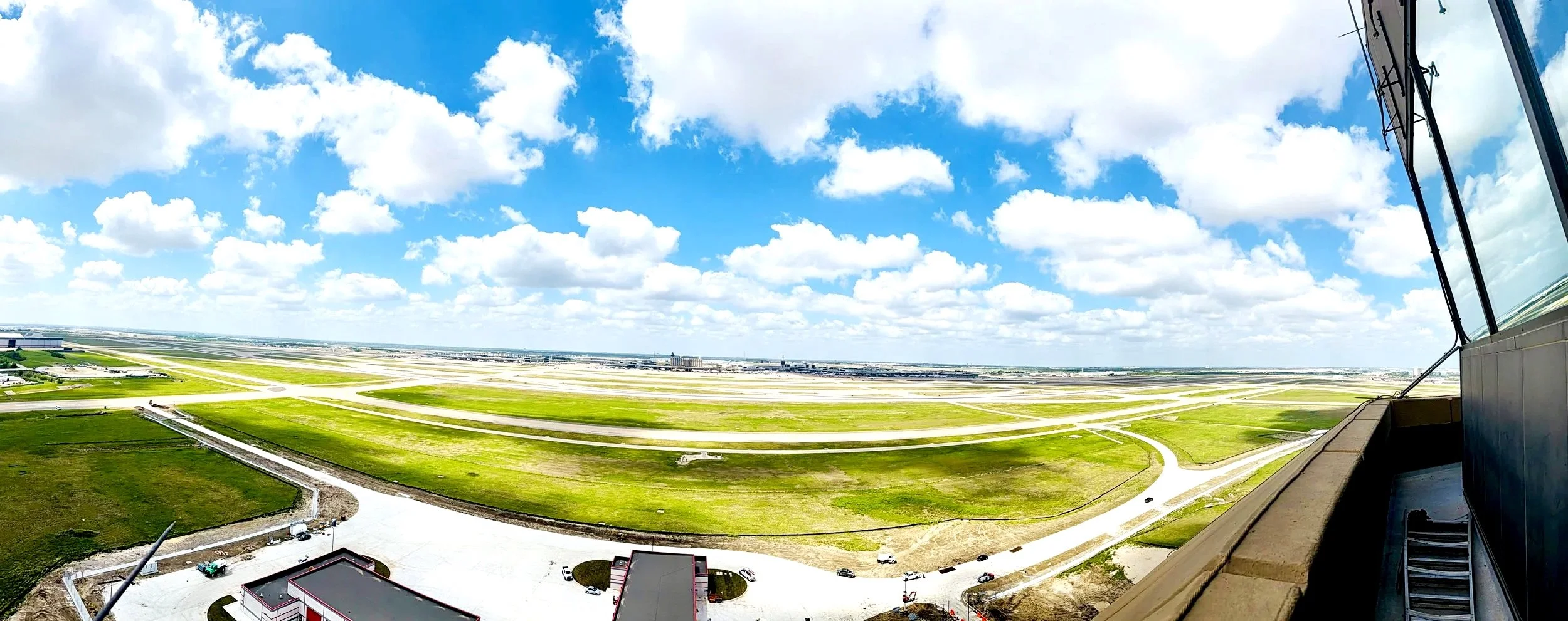 Aerial view of an airport with runways and taxiways, green grass areas, and partly cloudy sky seen from a building balcony.