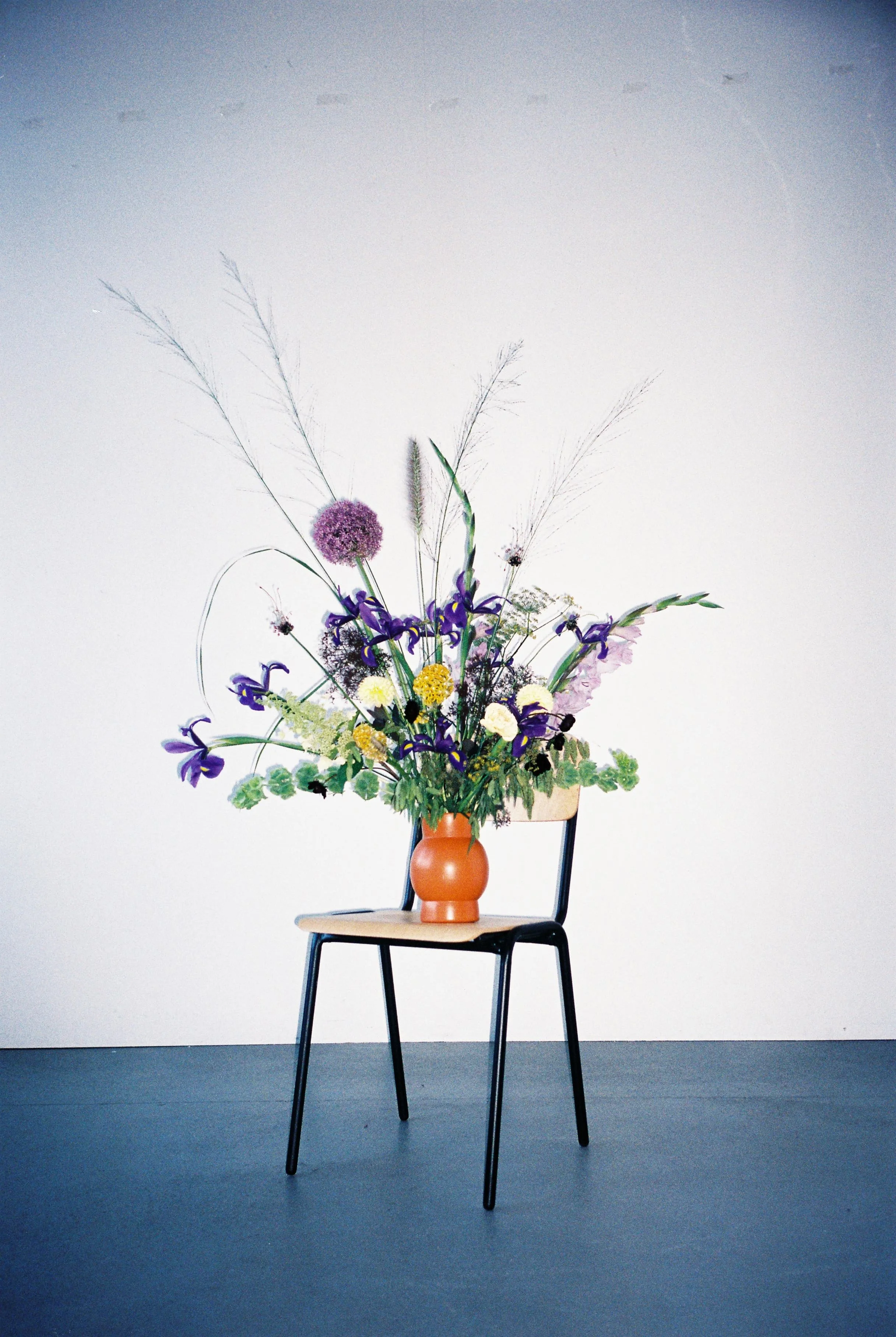 Ein Stuhl mit einer Vase voller bunter Blumen steht vor einer weißen Wand.