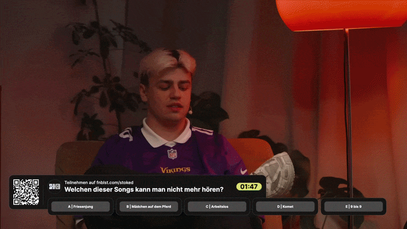 Ein junger Mann mit blondem Haar sitzt auf einem Sofa, trägt ein Vikings-Football-Trikot, und schaut nach unten, während im Hintergrund ein rotes Lampenlicht leuchtet.