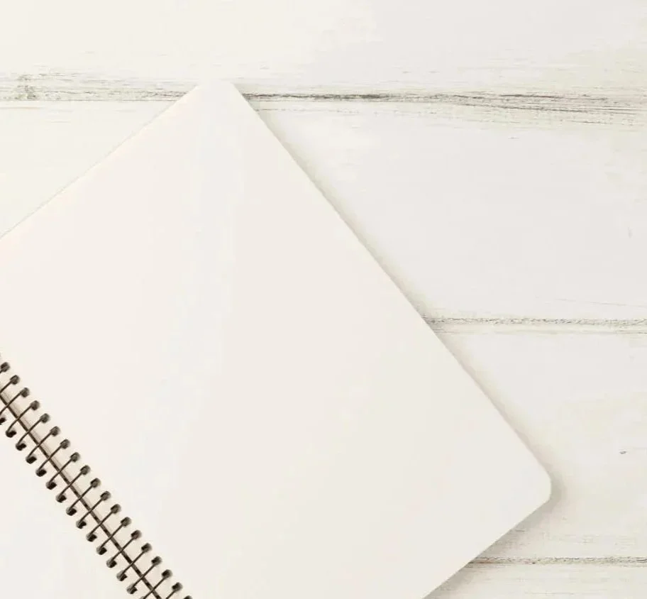 An open blank spiral notebook with a white cover on a white wooden surface.