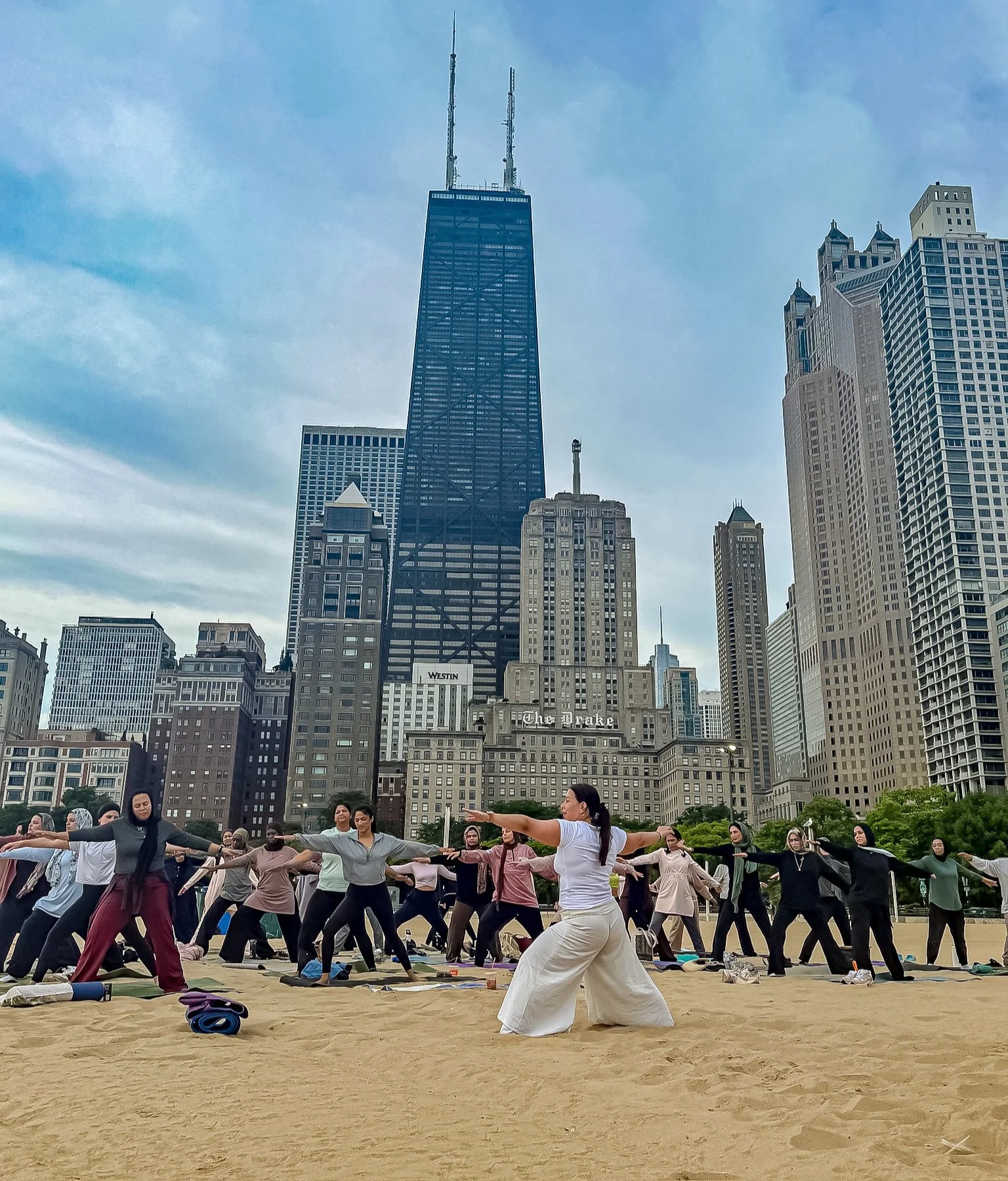 A large group of people participating in an outdoor yoga class in a park with the Chicago skyline, including the Willis Tower, in the background.