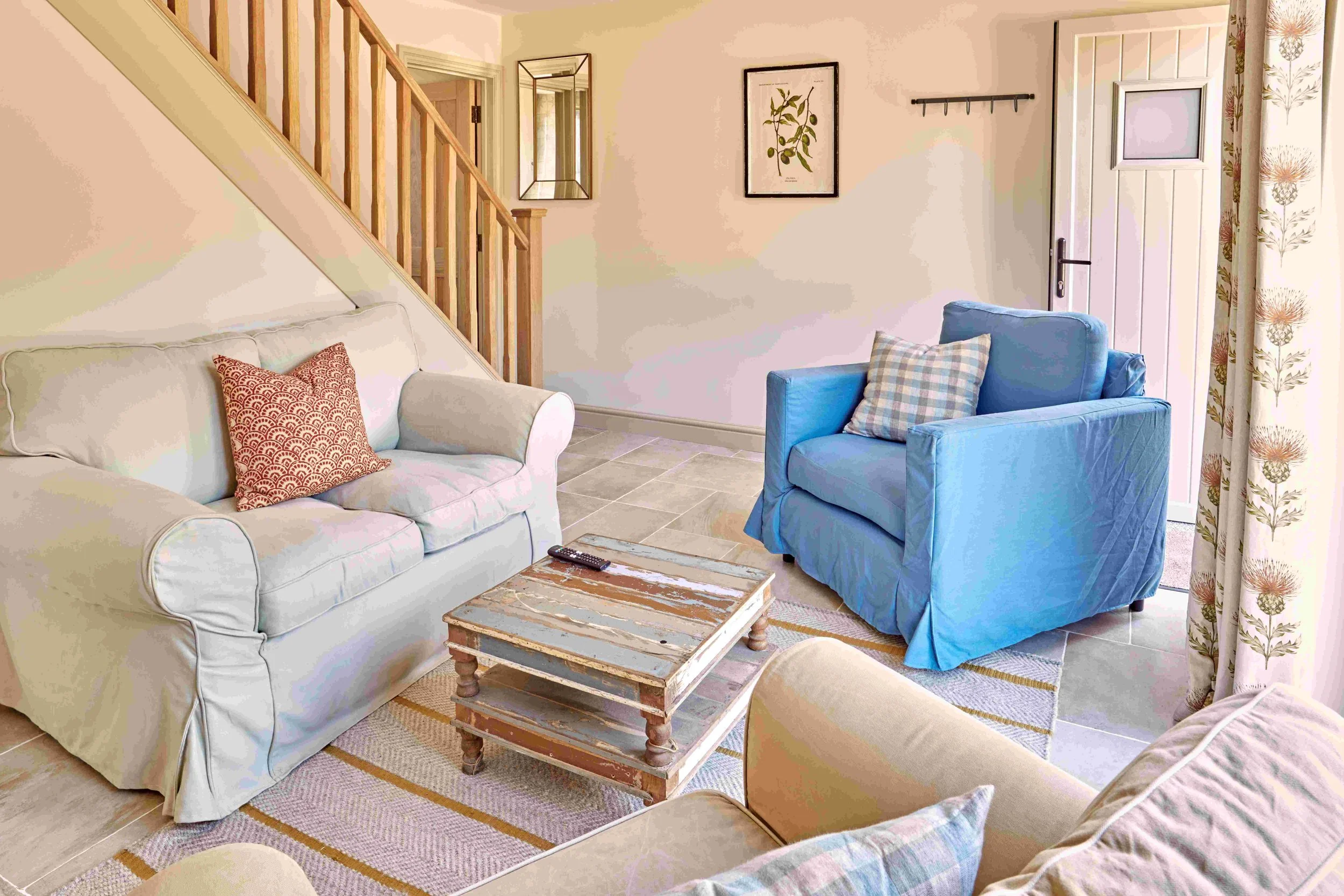 Living room with white sofa, blue armchair, rustic wooden coffee table, framed artwork, wall hooks, and floral curtains.