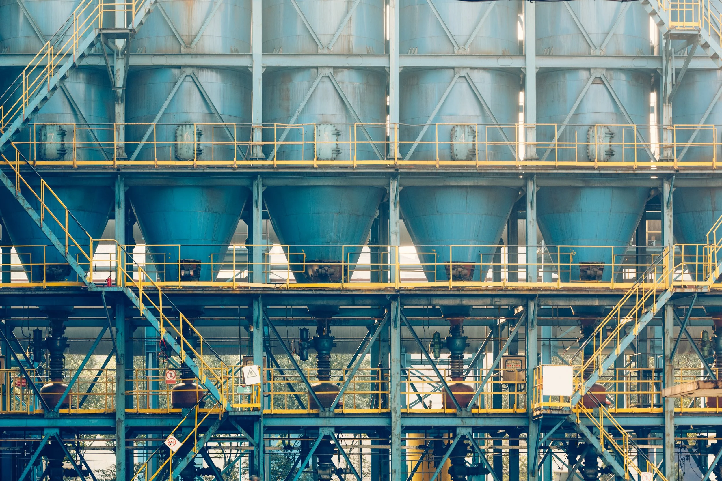 Structures industrielles avec réservoirs bleus, échelles jaunes et tuyaux.