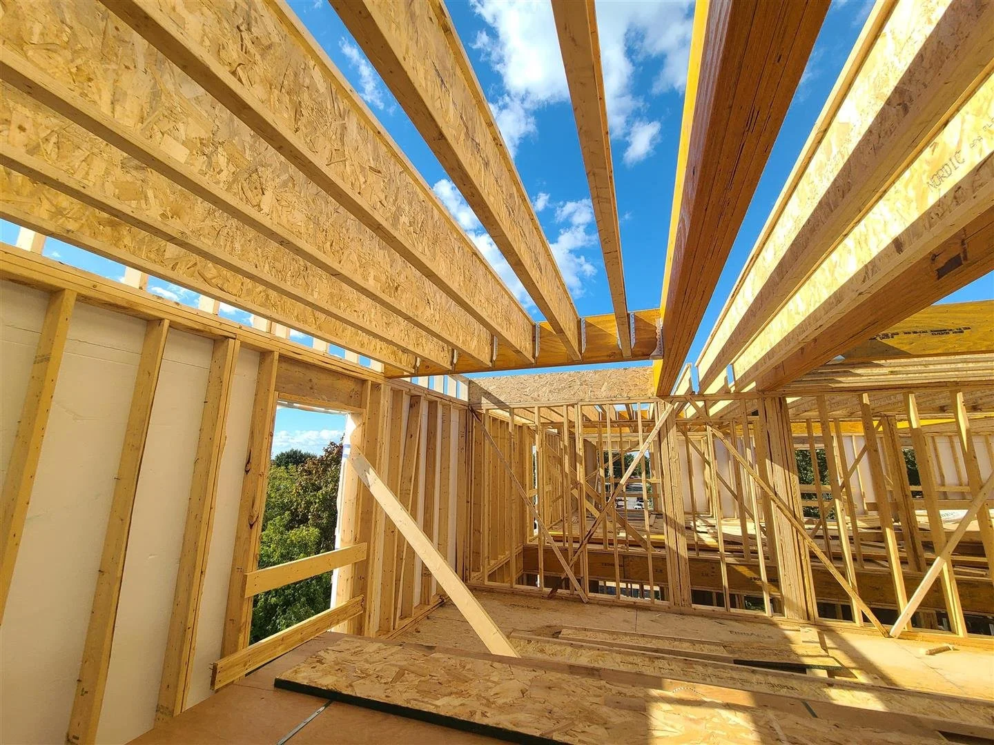 Construction en bois d'une maison avec un cadre en bois et des murs en panneaux. Le ciel bleu avec quelques nuages est visible à travers le toit en construction.