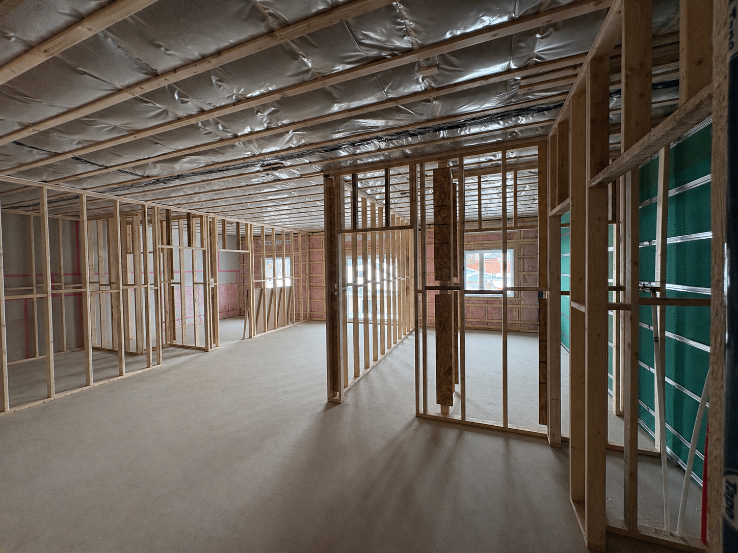 Intérieur d'une maison en construction, avec structure en bois, murs inachevés et fenêtres, plafond isolé.