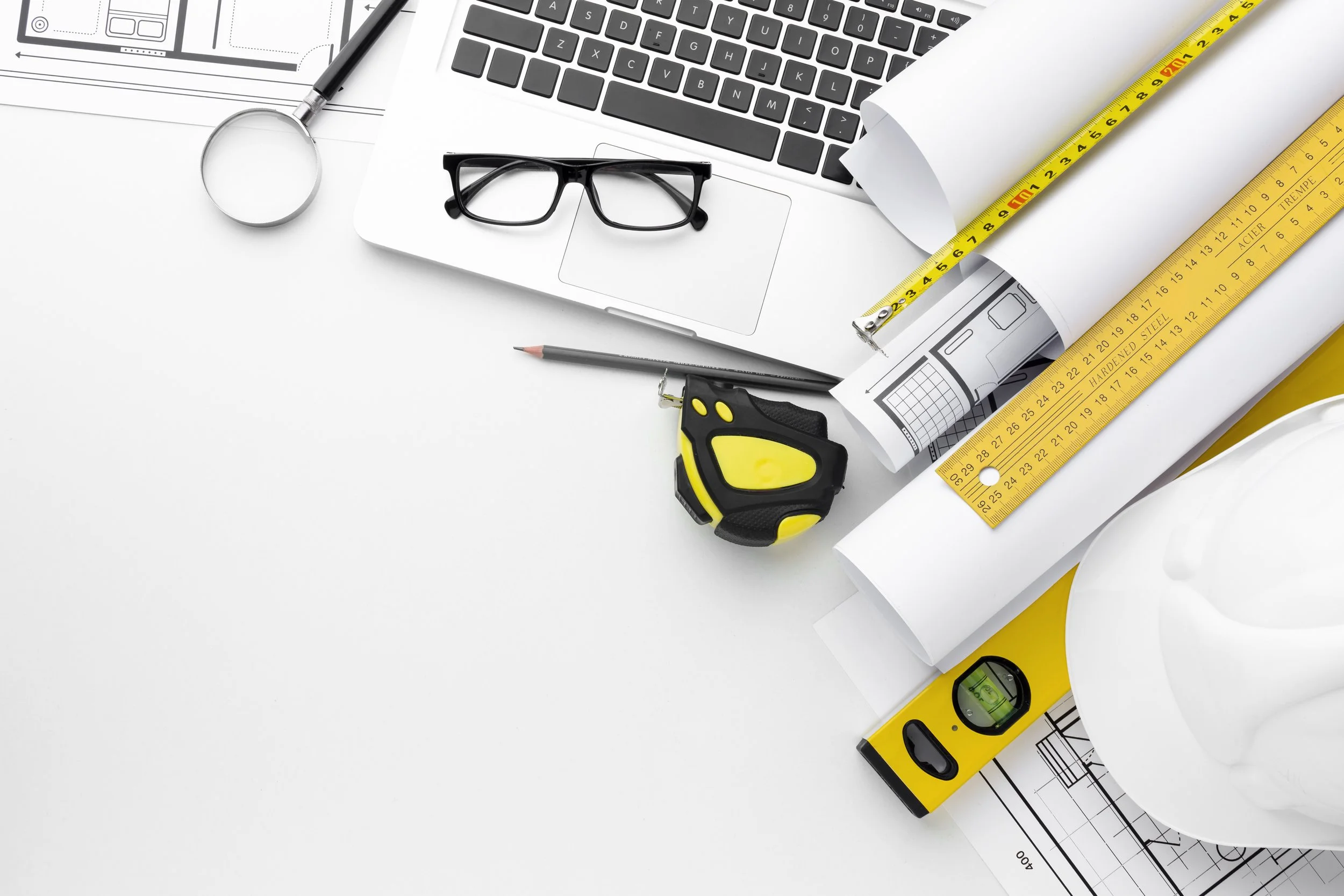 Outils de conception et de modélisation, y compris un ruban à mesurer, un niveau à bulle, des plans architecturaux, une paire de lunettes, un stylo, un ordinateur portable, une règle graduée, une fiche de dessin technique et un plan.