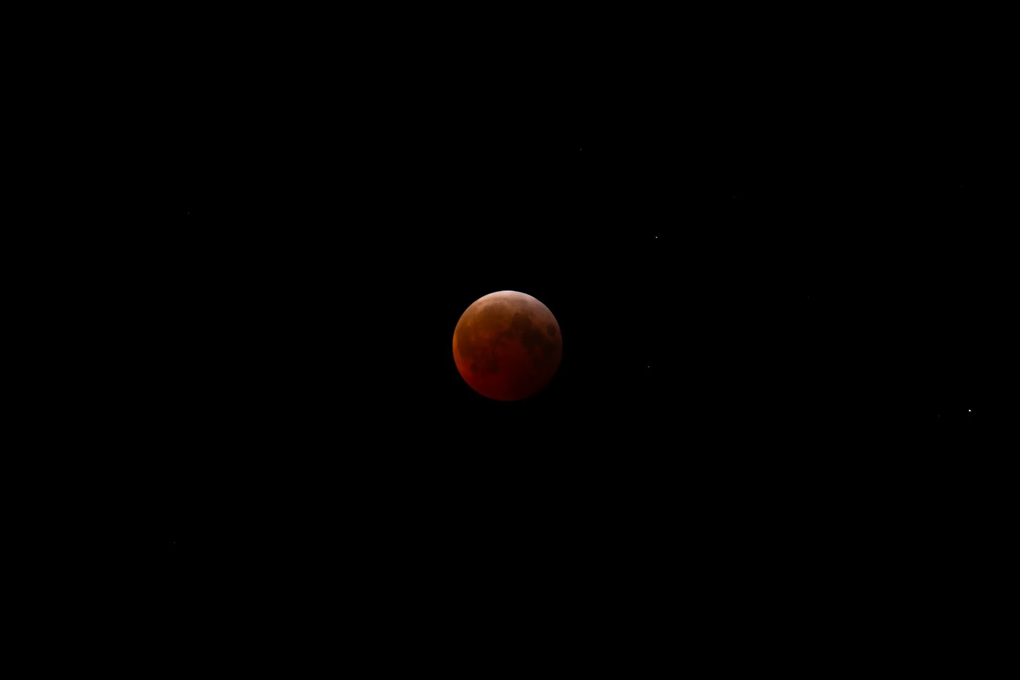 Dark red moon during a lunar eclipse against a black night sky with some stars.