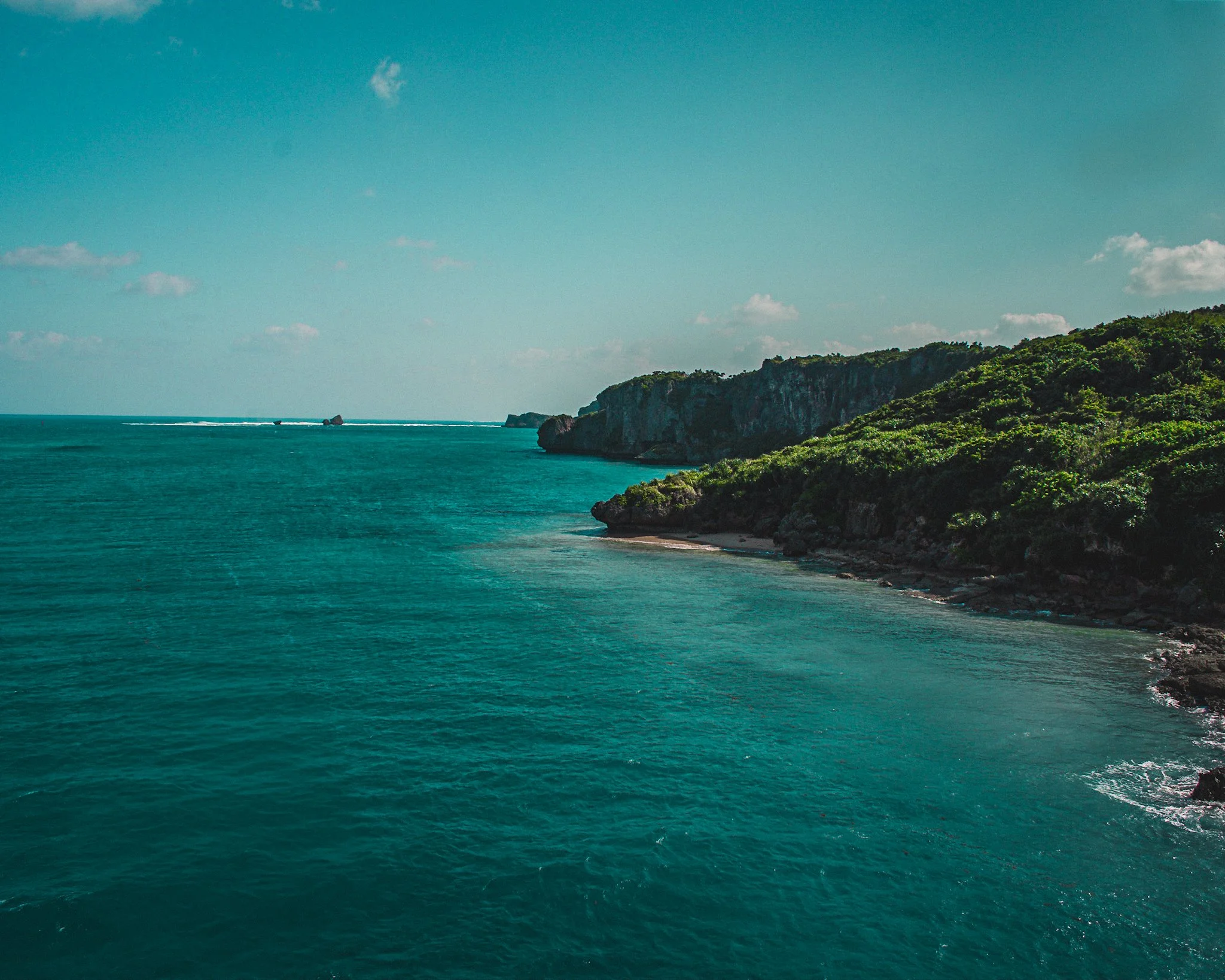 Ocean view with turquoise water, a coastline with green hills, and a partly cloudy sky.