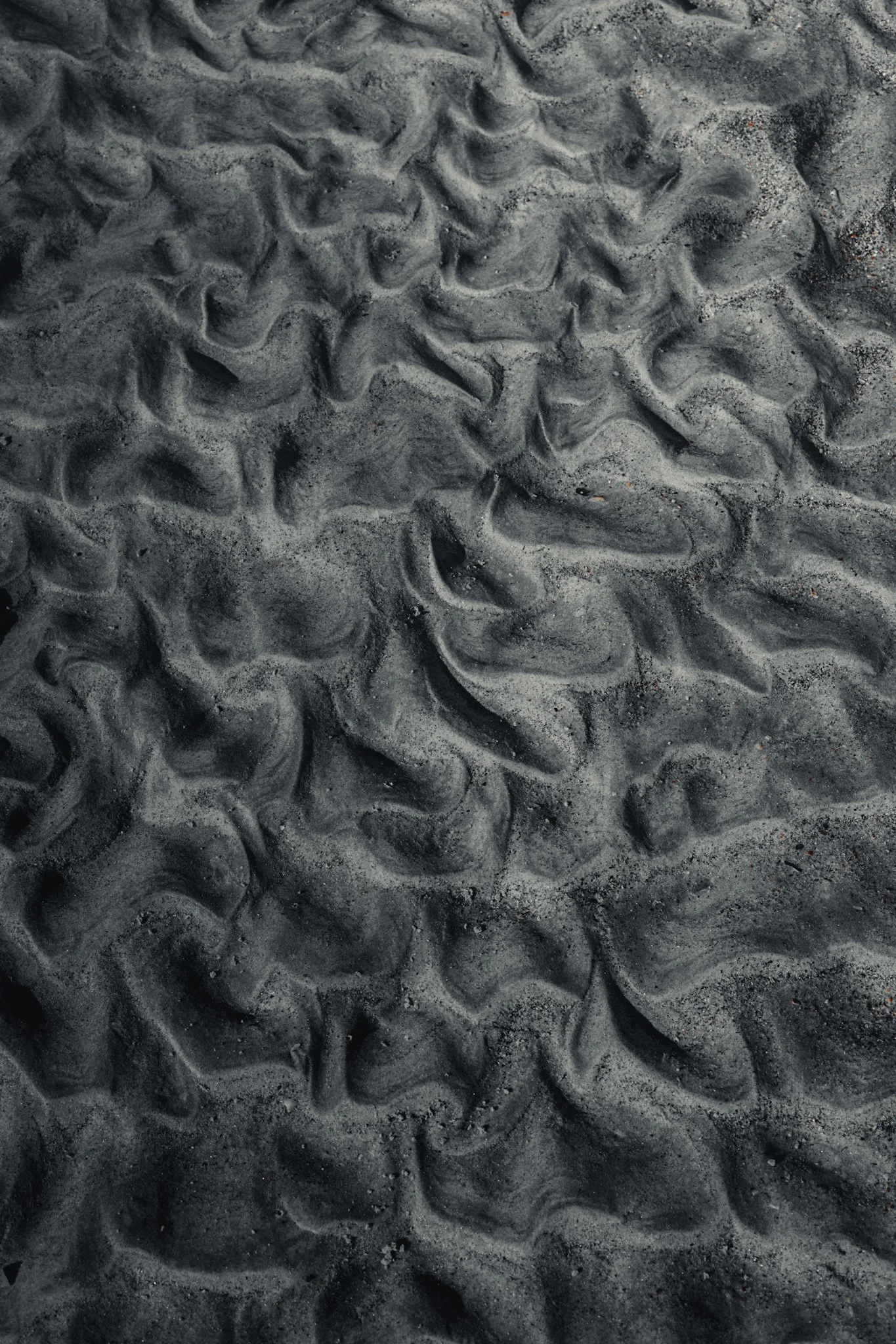 Close-up of dark gray and black sand with swirling and rippled patterns