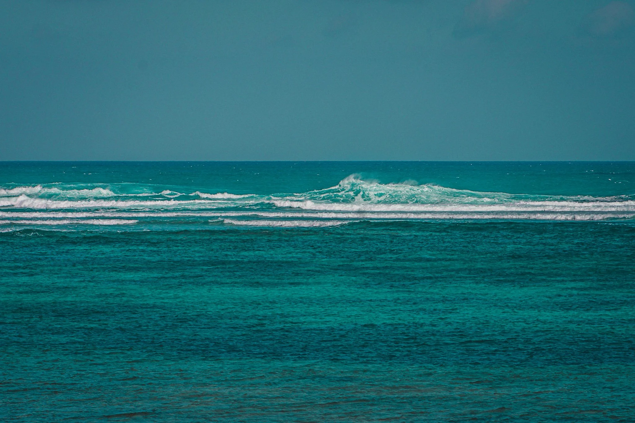 A view of the ocean with turquoise water and white waves, under a clear sky.