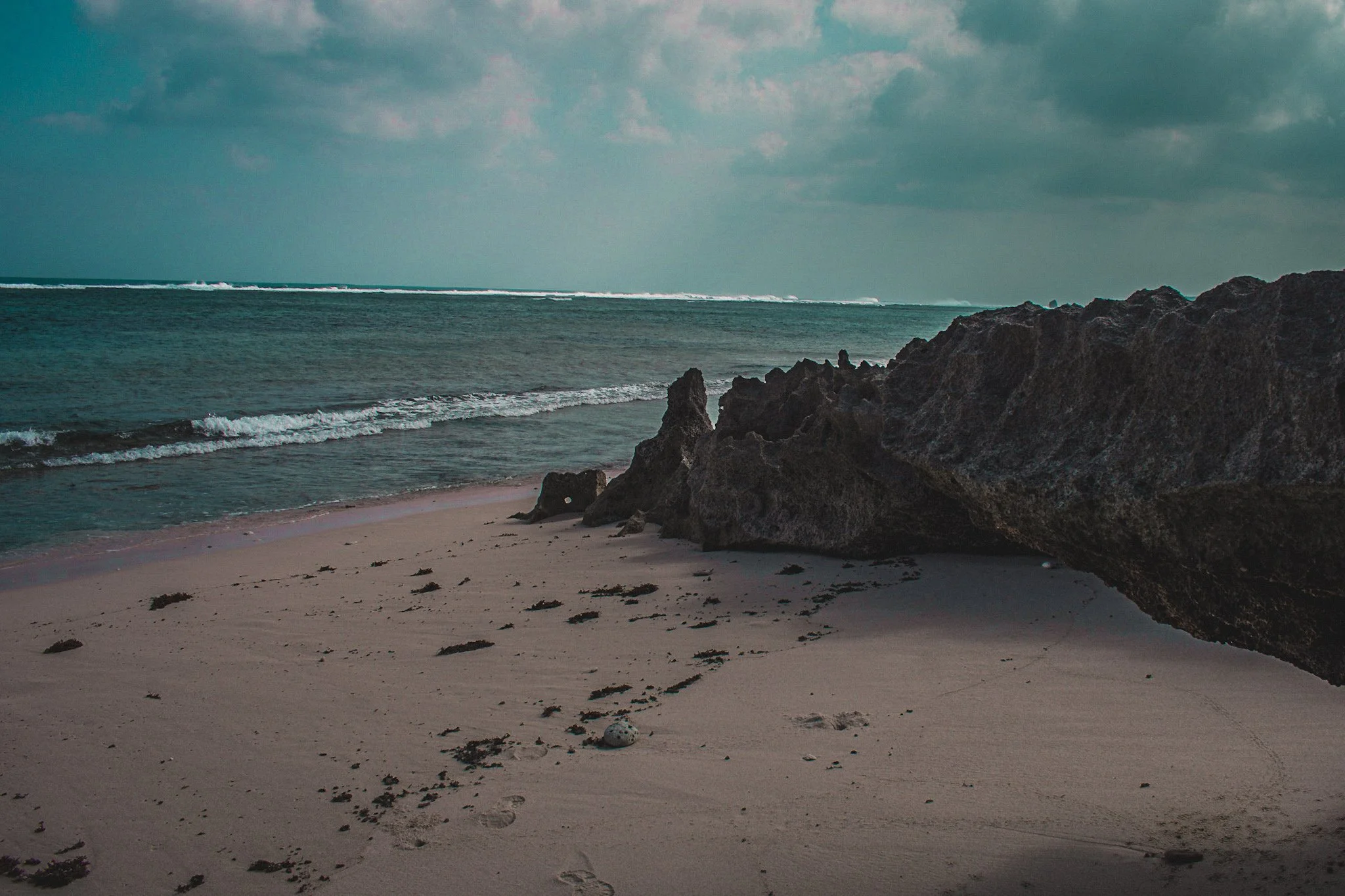 Beach with sandy shore, rocks, ocean waves, and cloudy sky