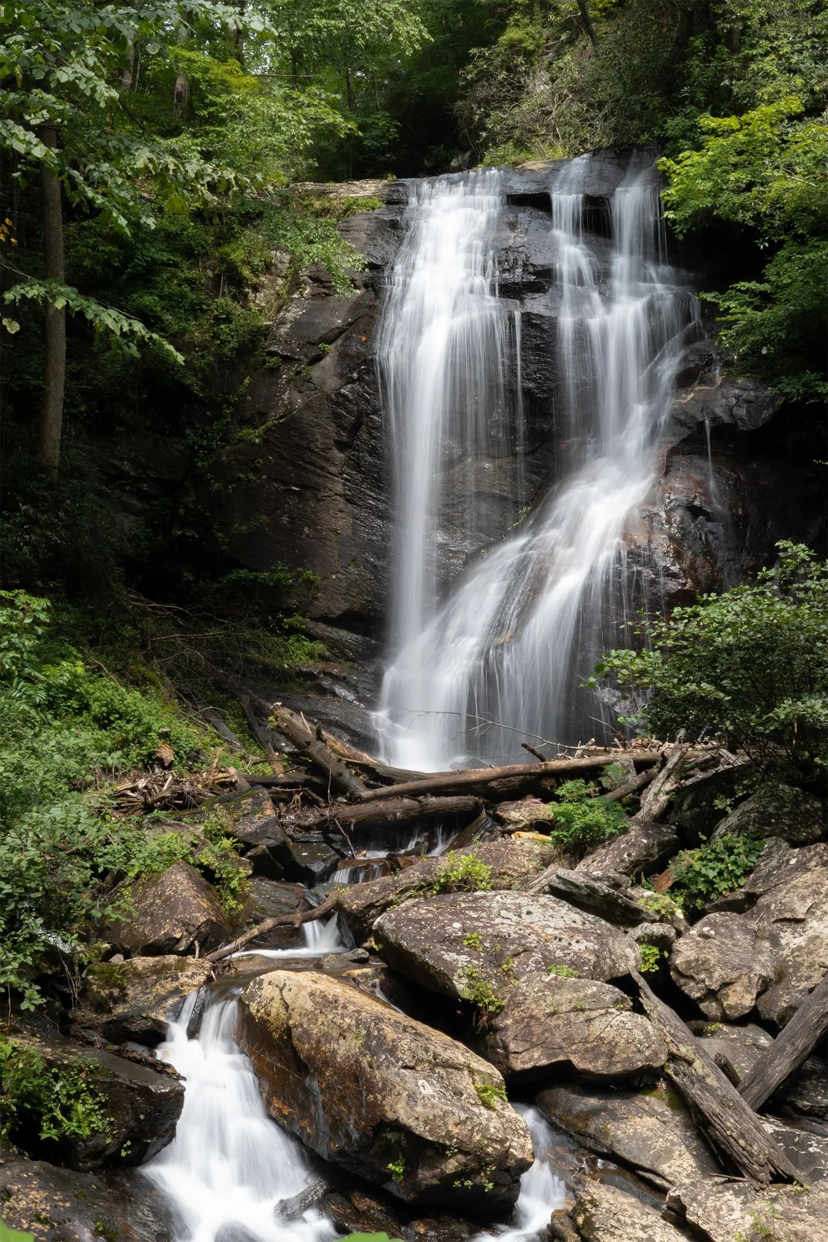 A multi-tiered waterfall flowing over rocks in a lush forest surrounded by green foliage.