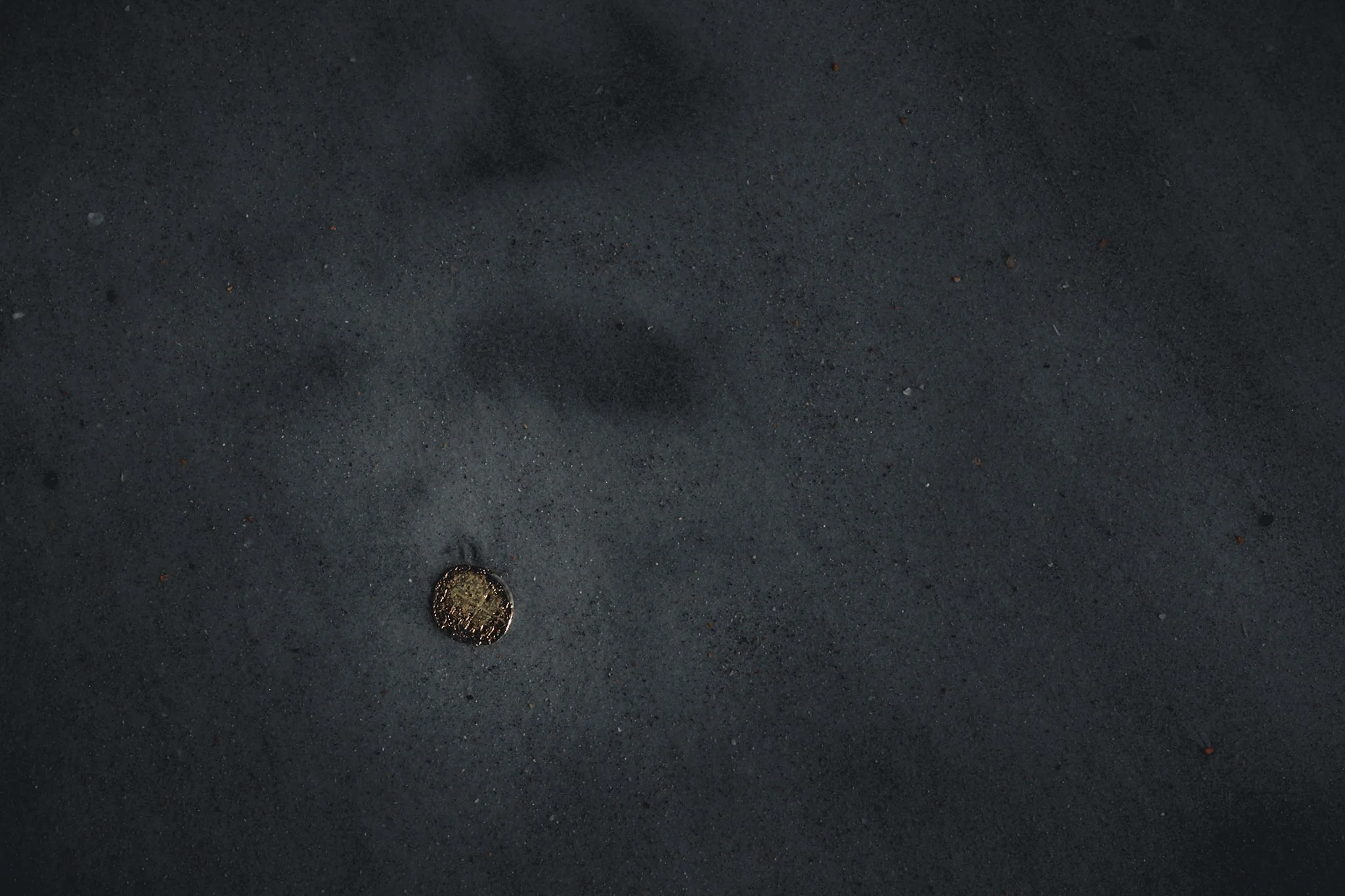 A dark sand or gravel surface with a gold-colored coin near the bottom of the image.