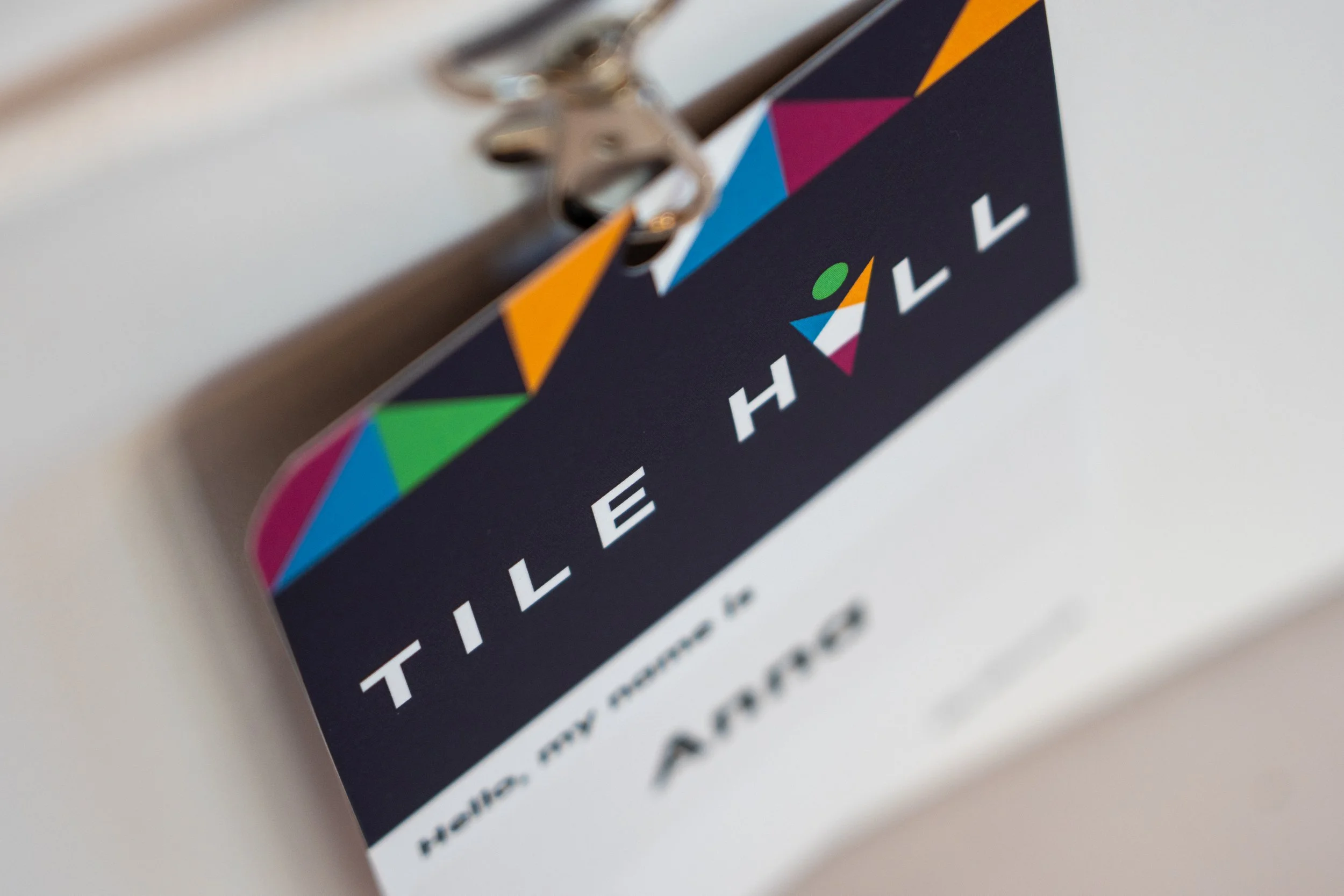 Close-up of a black event badge with colorful triangular designs and white text, attached to a keychain.