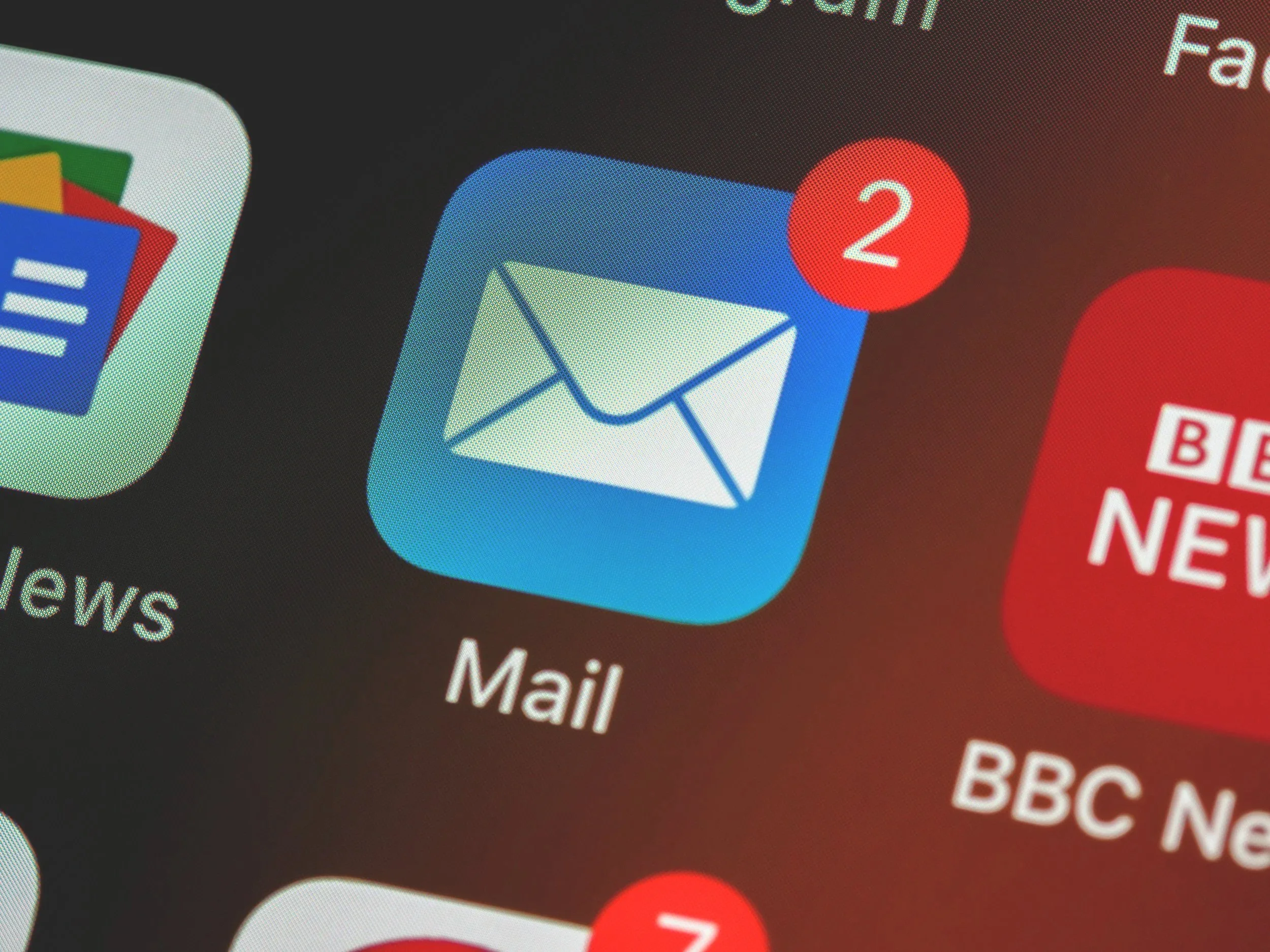Close-up of a smartphone screen showing app icons for mail, news, and messaging with notification badges, including a red circle with the number 2 for emails.