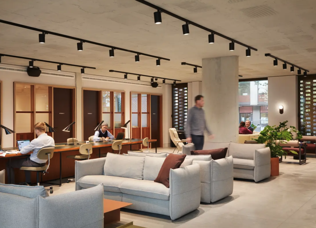 Modern co-working space or office lobby with seating areas, desks, and people working or meeting inside.