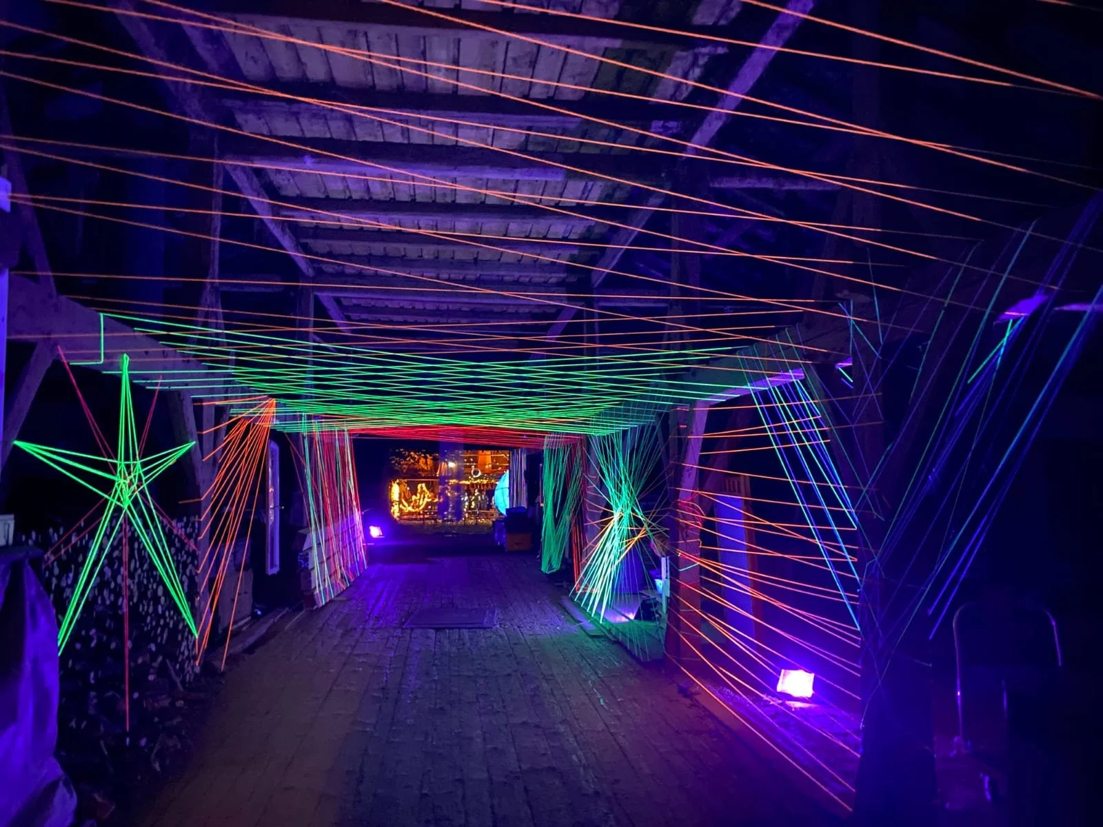A tunnel decorated with colorful, glowing neon light art, featuring stars and geometric shapes under a wooden ceiling.