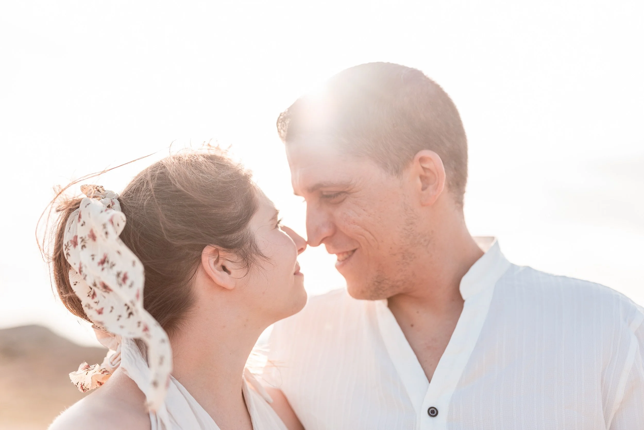 Una pareja mira con cariño y ternura, con la frente casi tocándose, en un entorno brillante y soleado, en un momento romántico y afectuoso.
