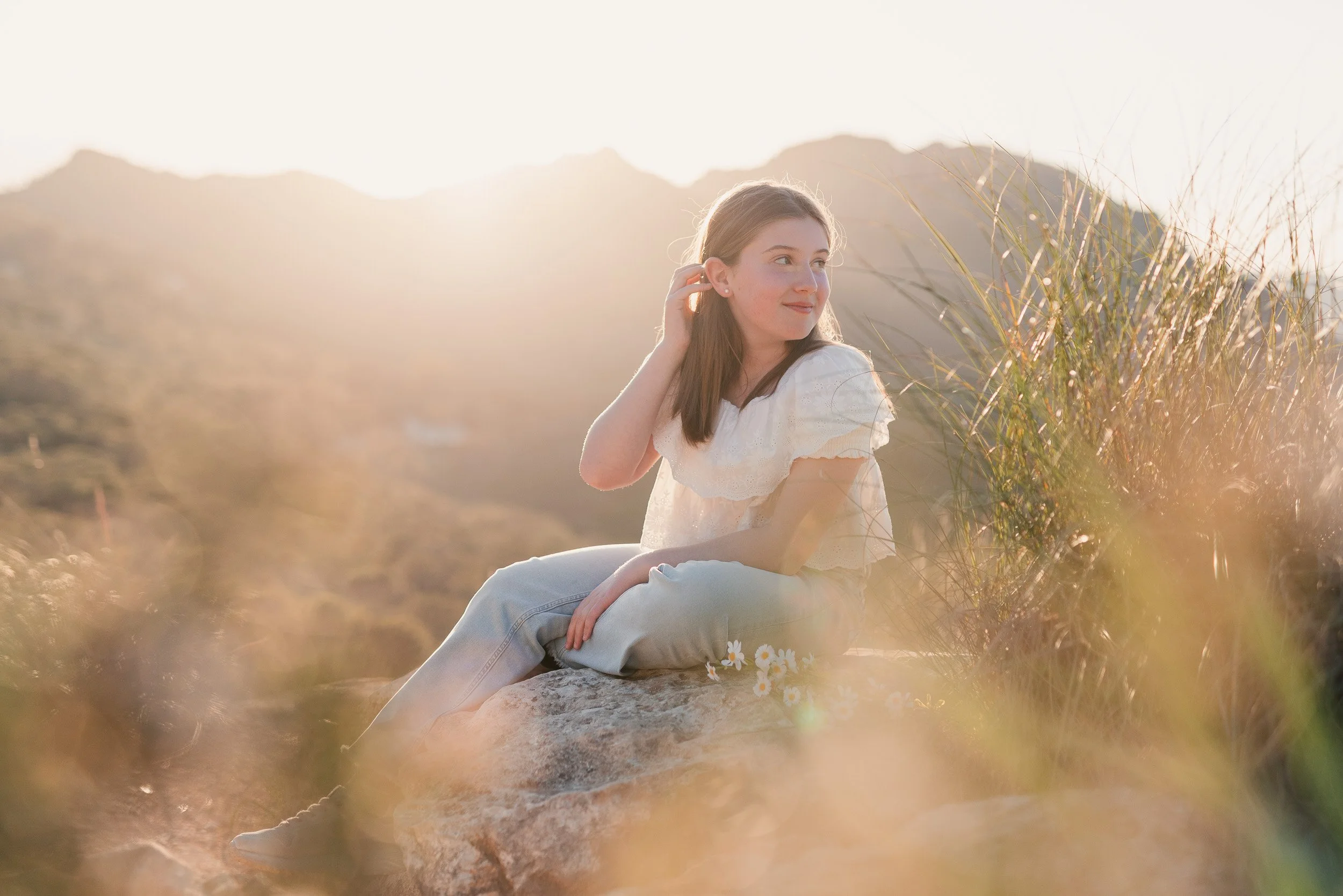 Niña sentada en una roca en un campo de hierba en la luz del atardecer.