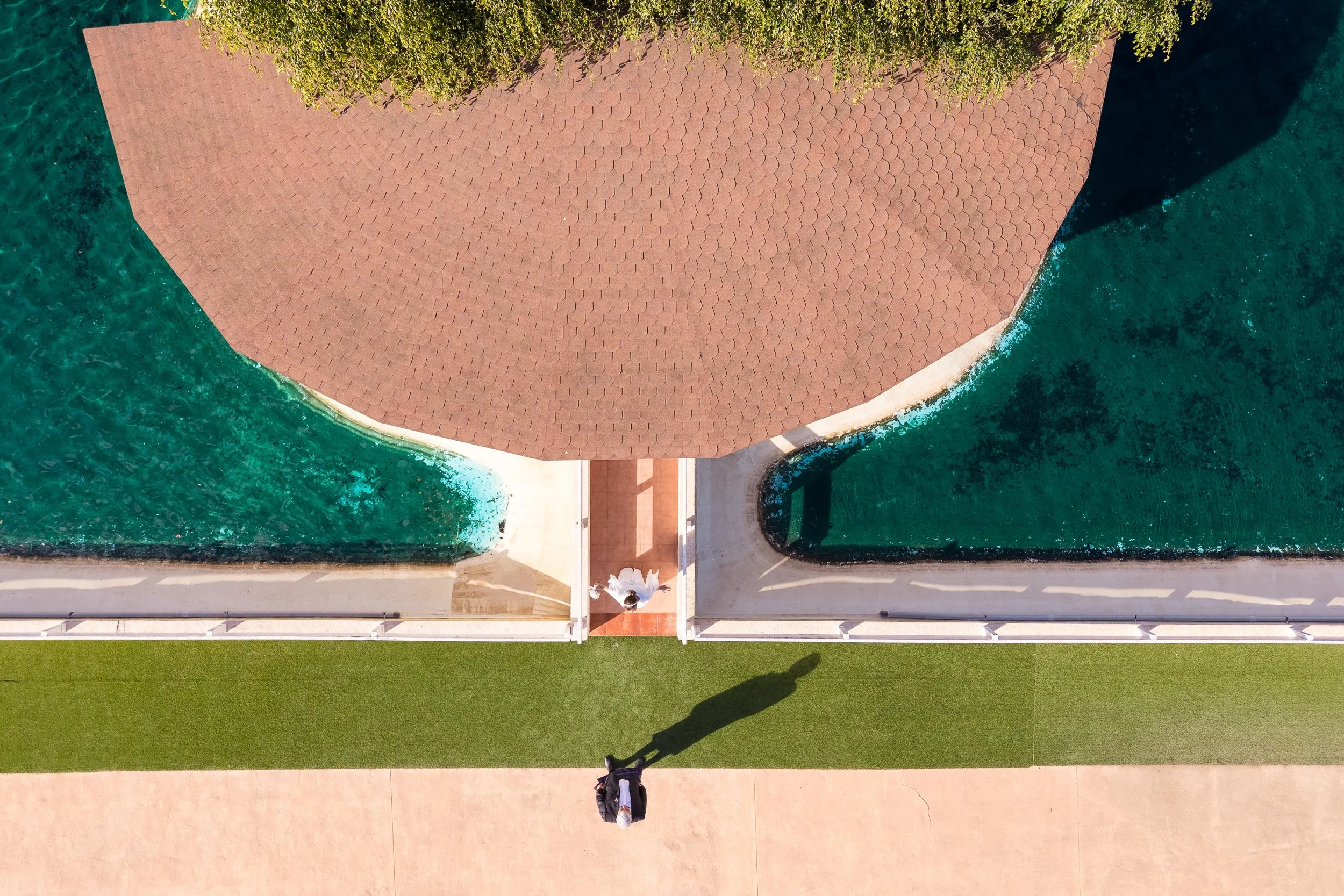Vista aérea de un área construida en un lago con áreas verdes y una estructura en forma de rombo o diamante, con los novios uno enfrente de otro.