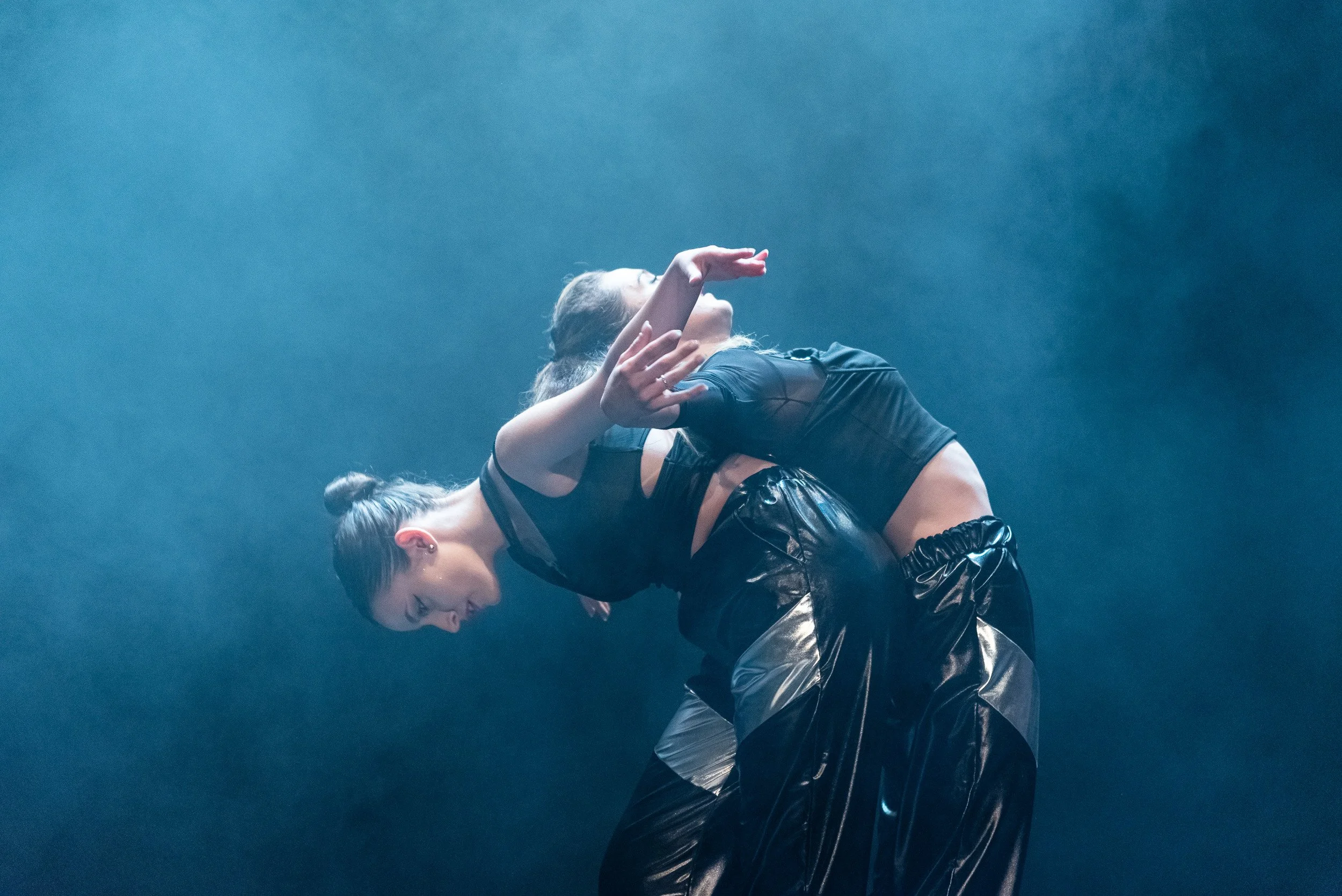Dos mujeres bailando en una actuación de danza moderna en un escenario con iluminación azul.