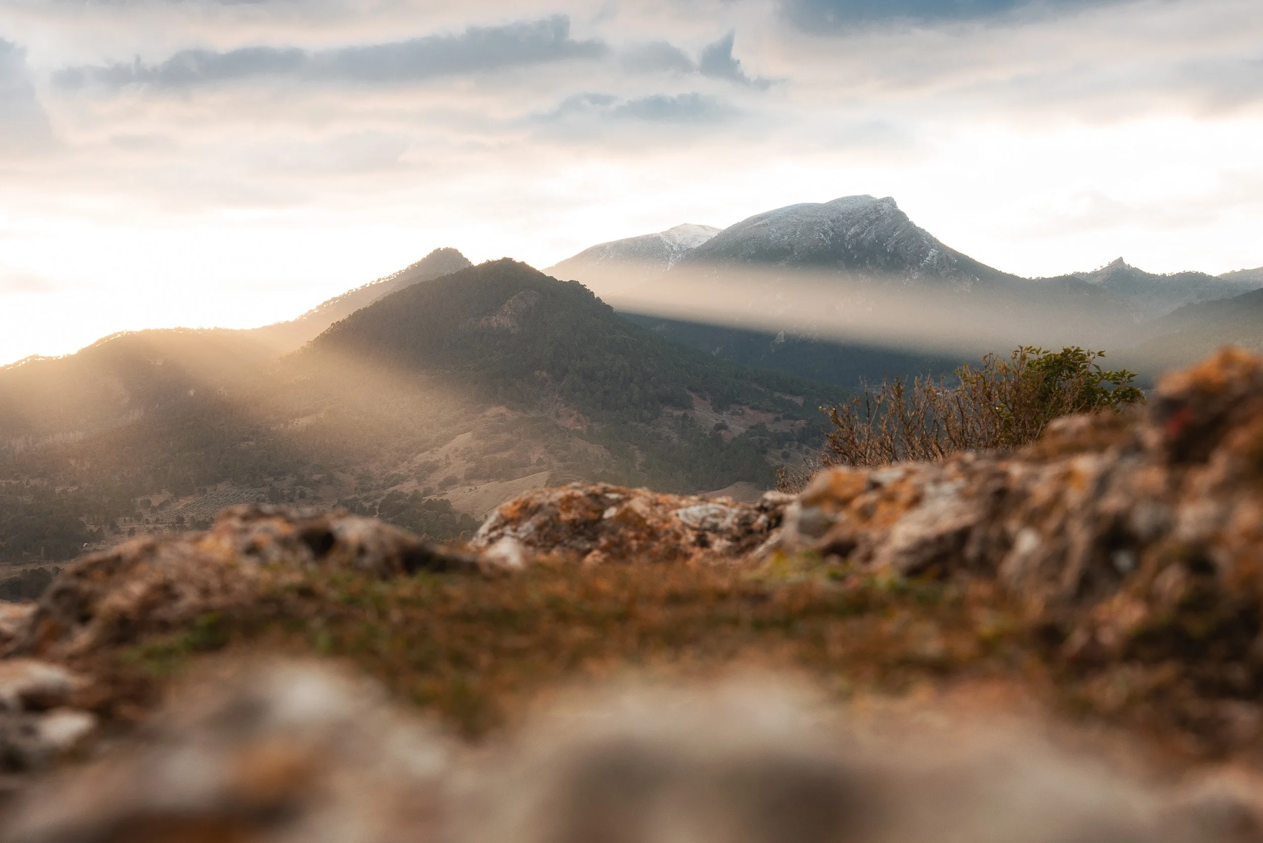 Montañas nevadas al atardecer con nubes y luz solar.