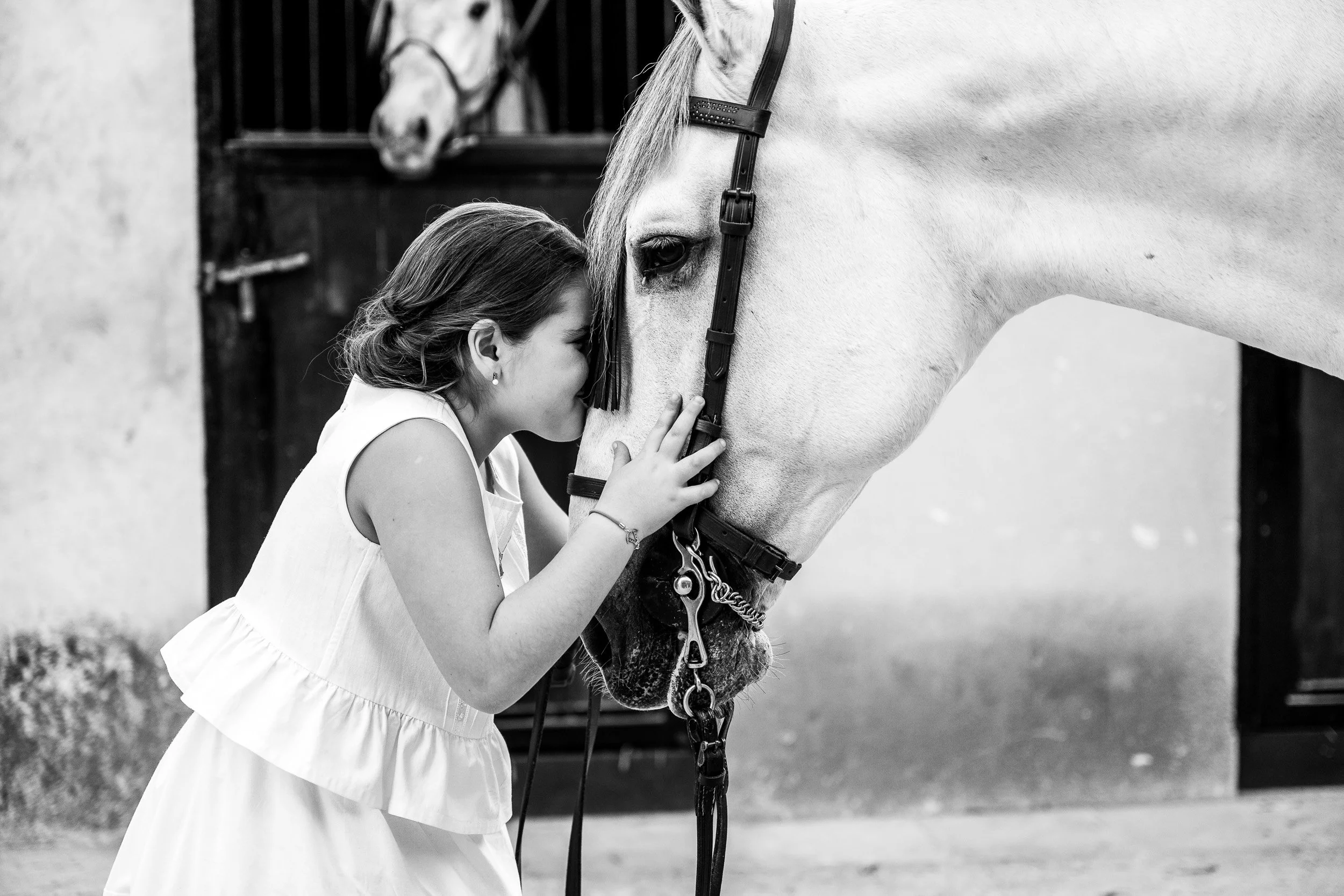 Joven mujer acaricia la cara de un caballo blanco en un establo, en blanco y negro.