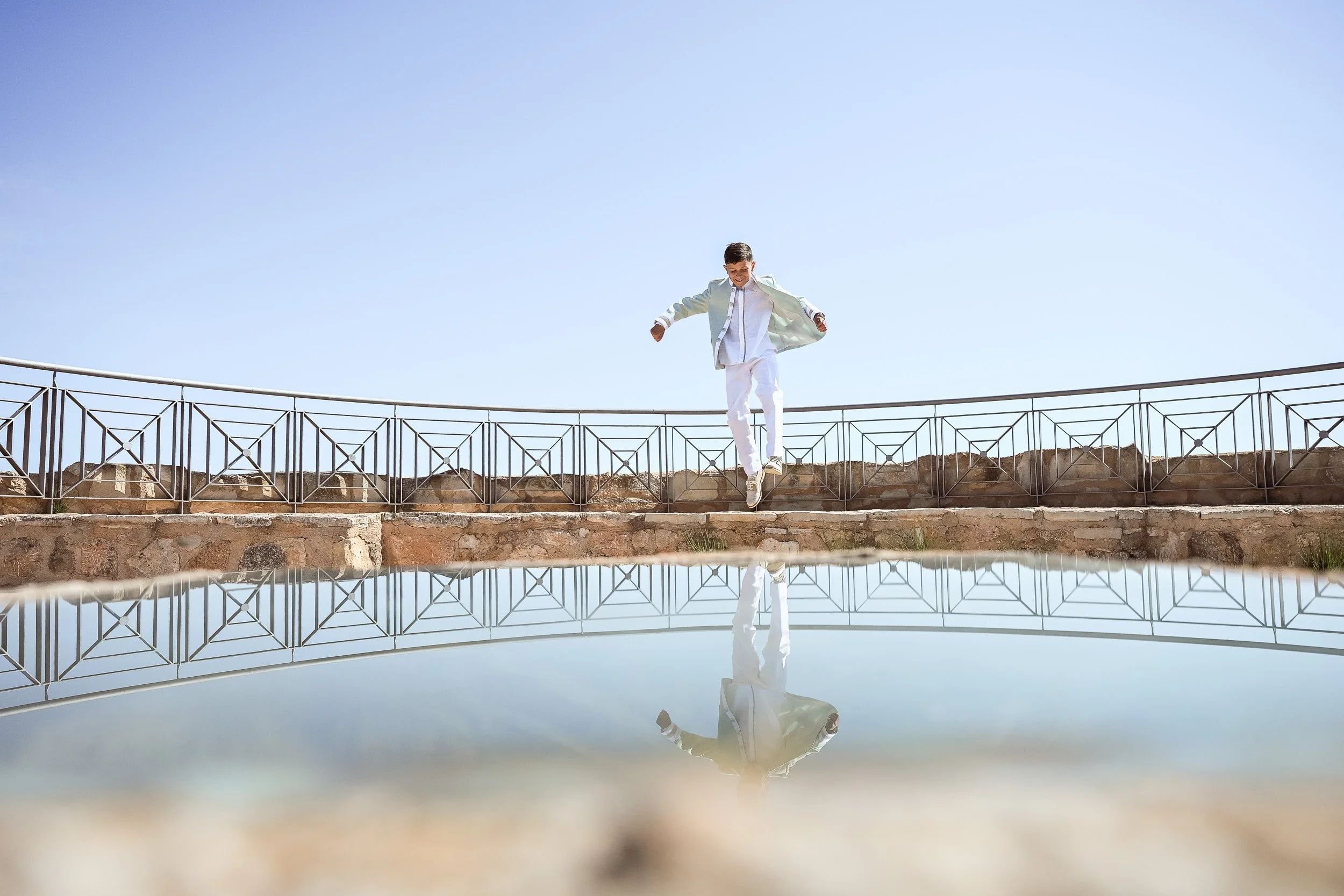 Niño con traje de comunión saltando desde una plataforma, siendo reflejado en la parte inferior por un cristal.