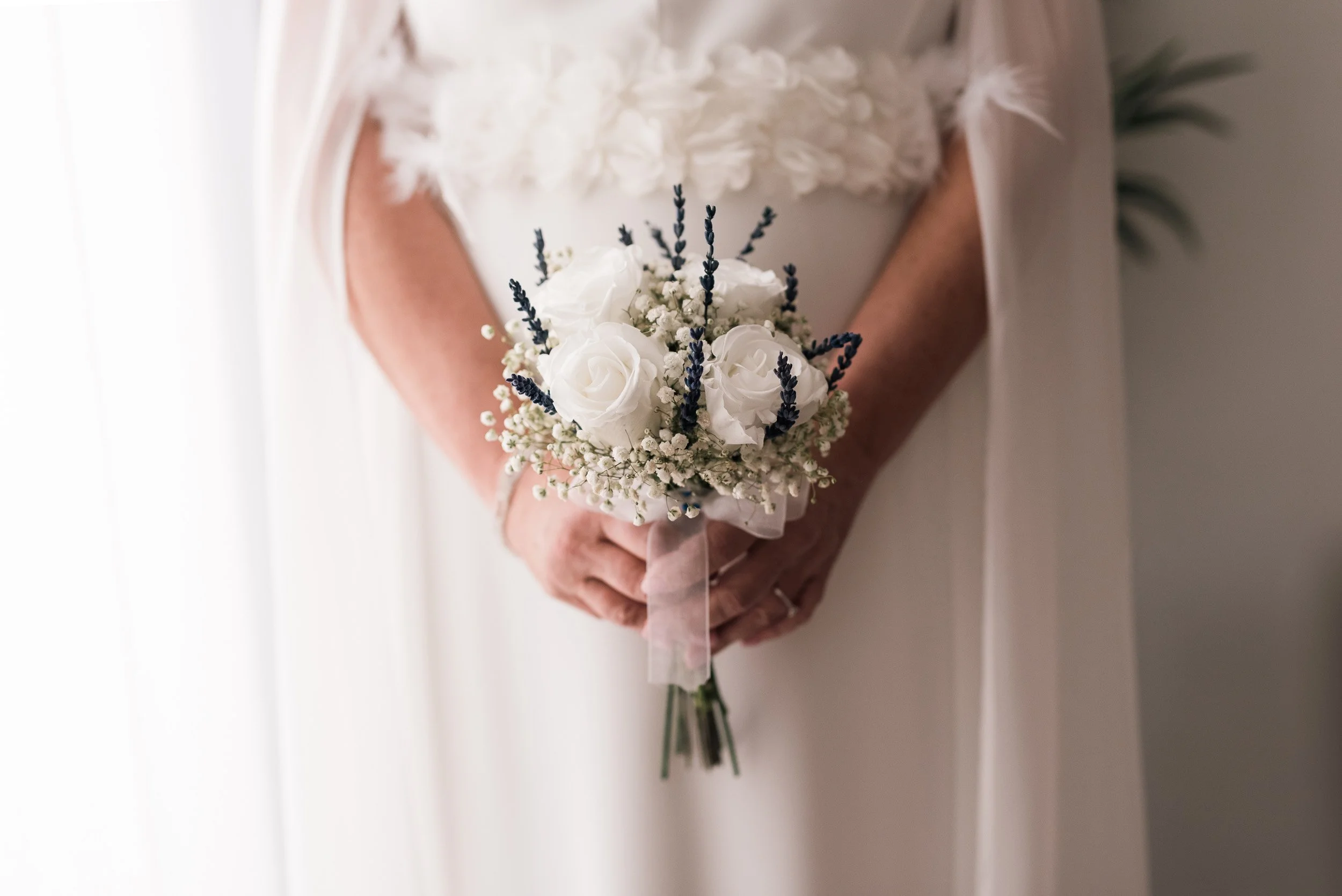 Persona sosteniendo un ramo de flores blancas y lavanda, vestido de bodas.