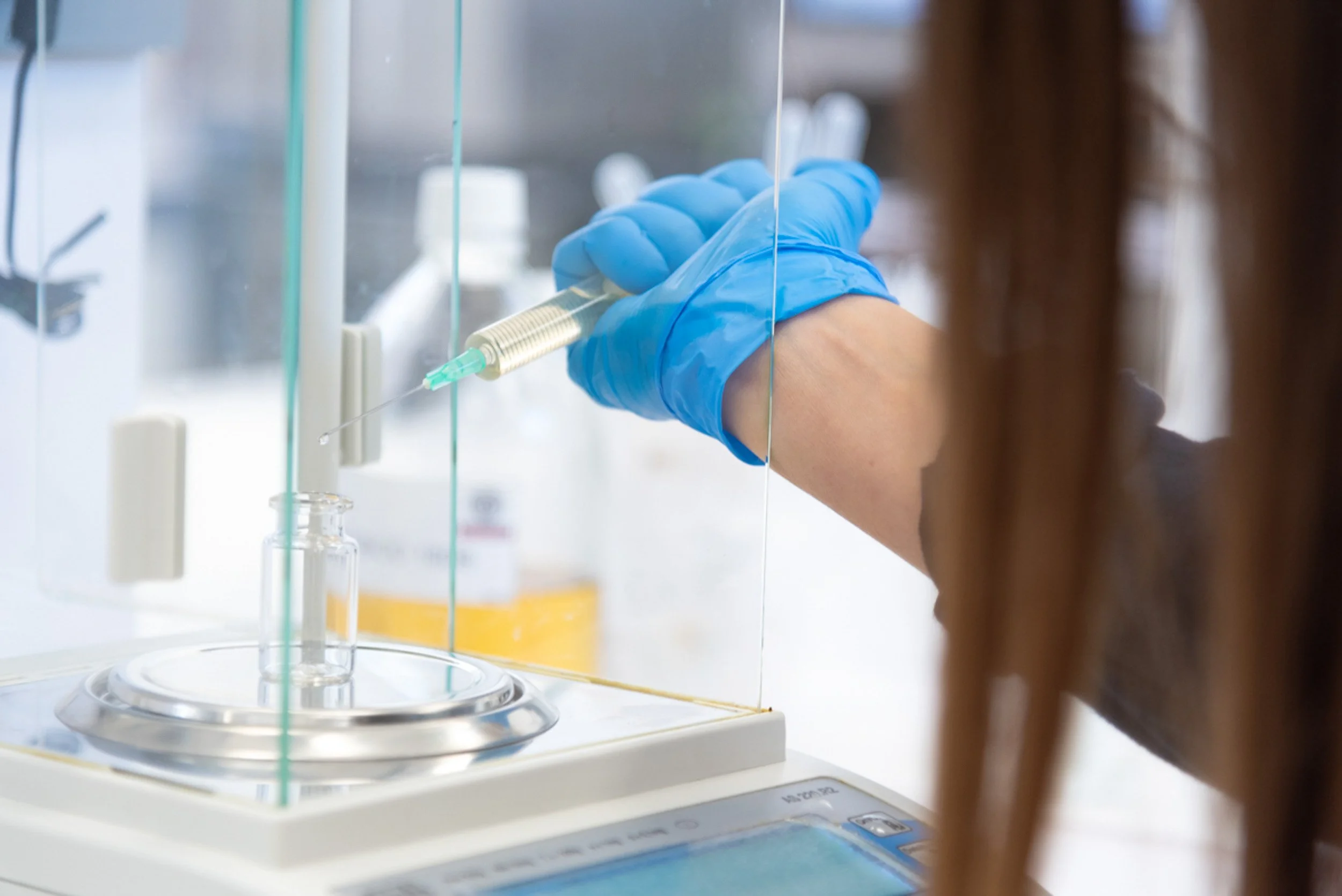 Una mano con guantes azules insertando una aguja en una máquina de laboratorio.