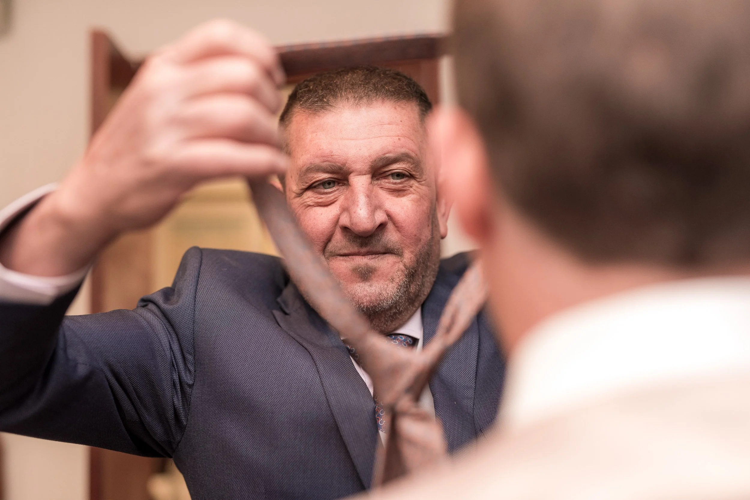 Hombre con saco y corbata, haciendo forma de un círculo con sus manos, en un entorno interior.