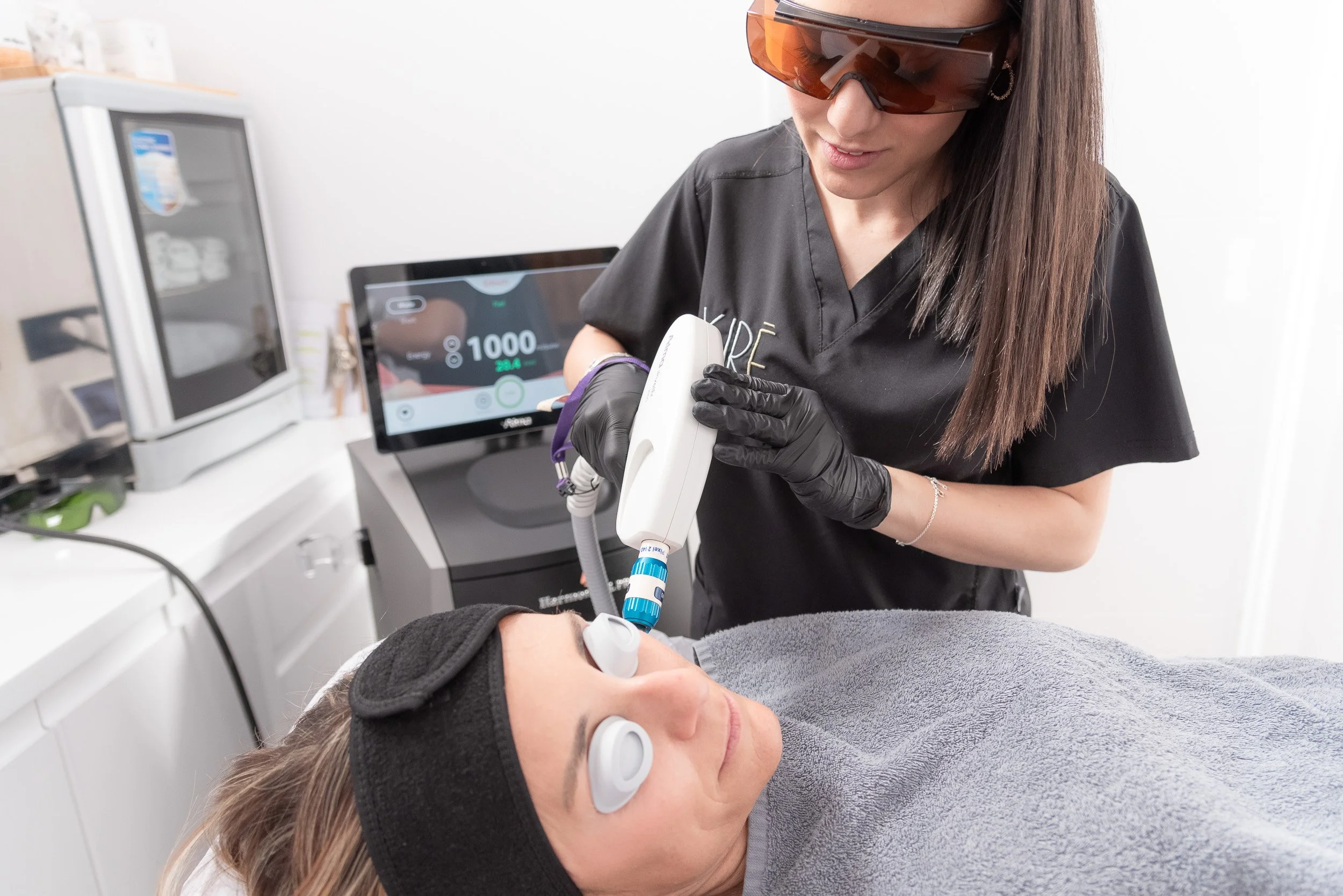 Médico tratando a un paciente en una clínica estética, con equipo médico y una pantalla digital en el fondo.
