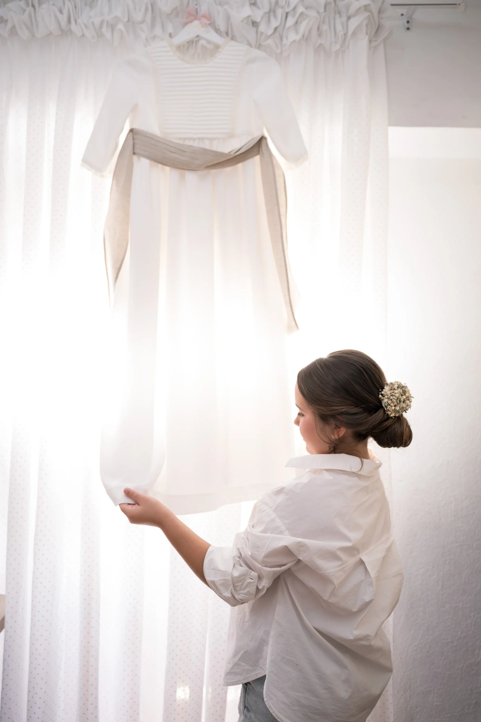 Mujer colocando un vestido blanco en una ventana con cortinas blancas.