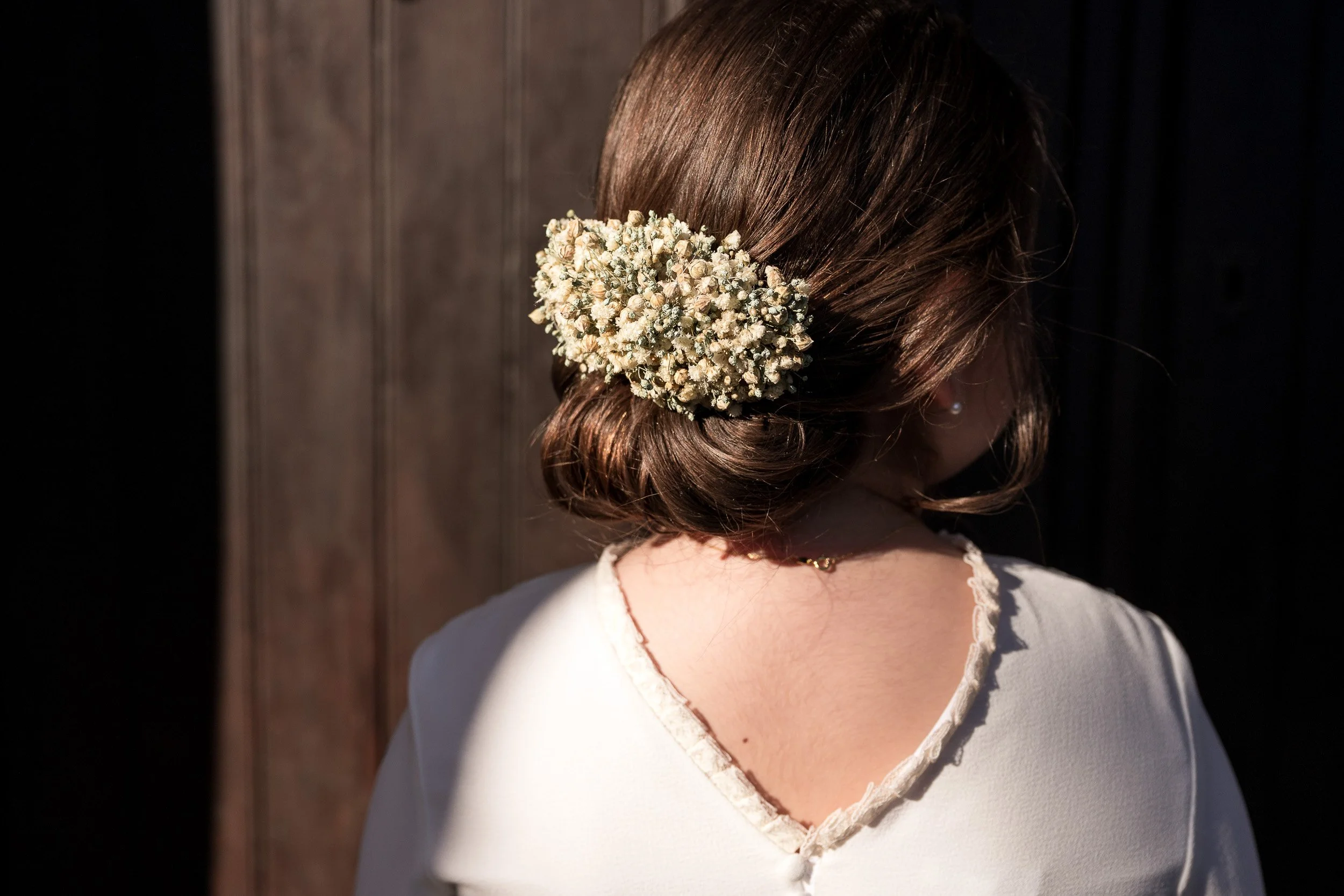 Mujer vista desde atrás con peinado recogido decorado con ramo de pequeñas flores blancas.