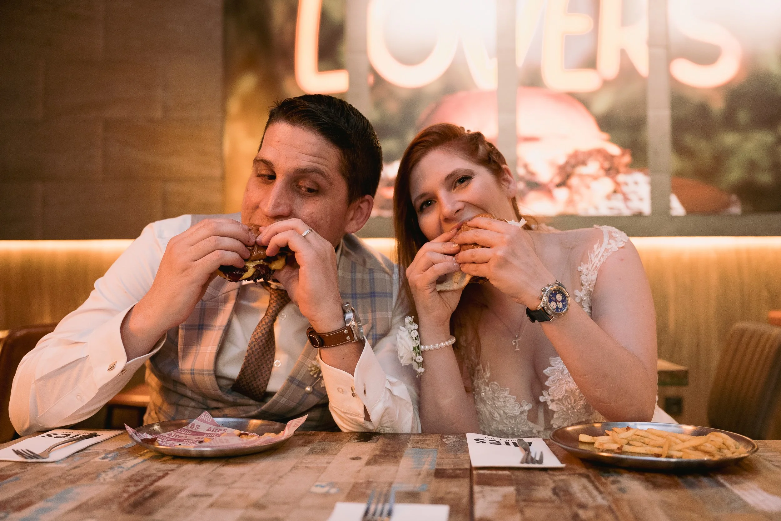 Una pareja vestida de boda comiendo hamburguesas en un restaurante.