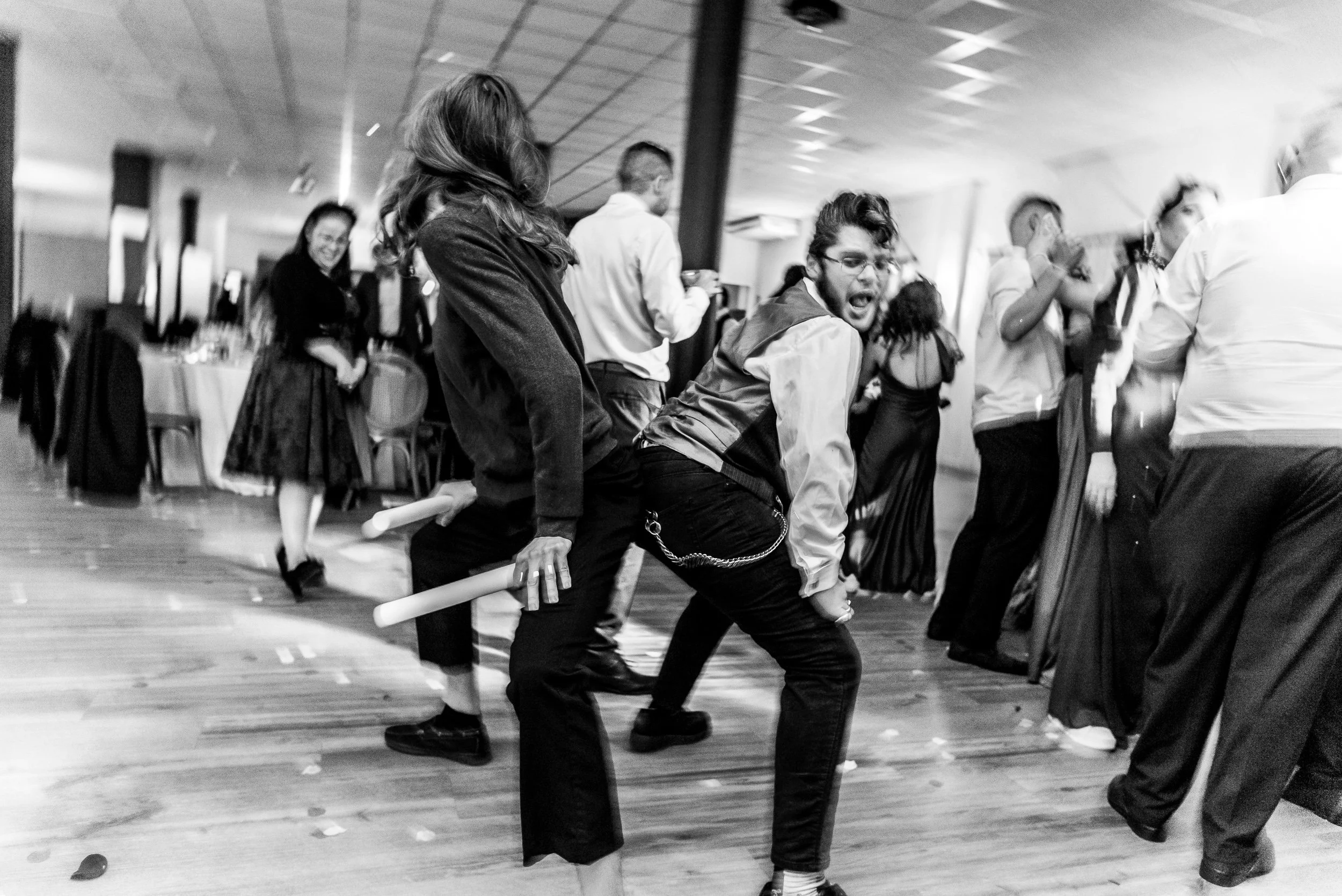 Personas en un salón bailando, disfrazados con prendas oscuras, formando una fila, en una fiesta o evento social.
