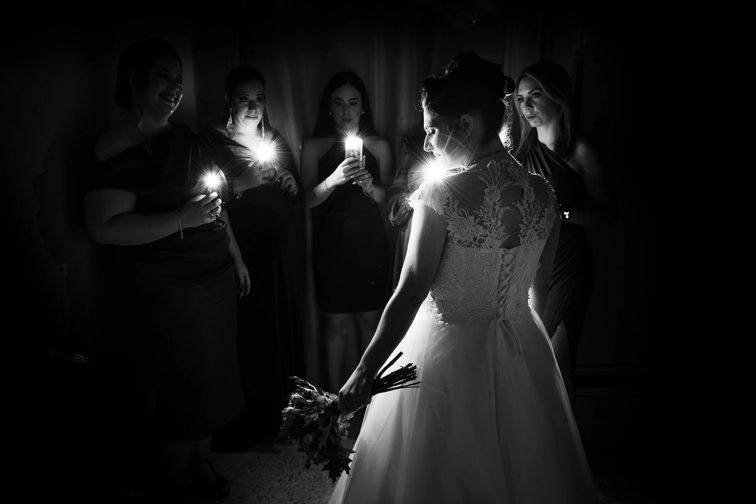 Mujer vestida con vestido de boda, rodeada de cinco damas de honor que sostienen velas encendidas en un entorno oscuro.