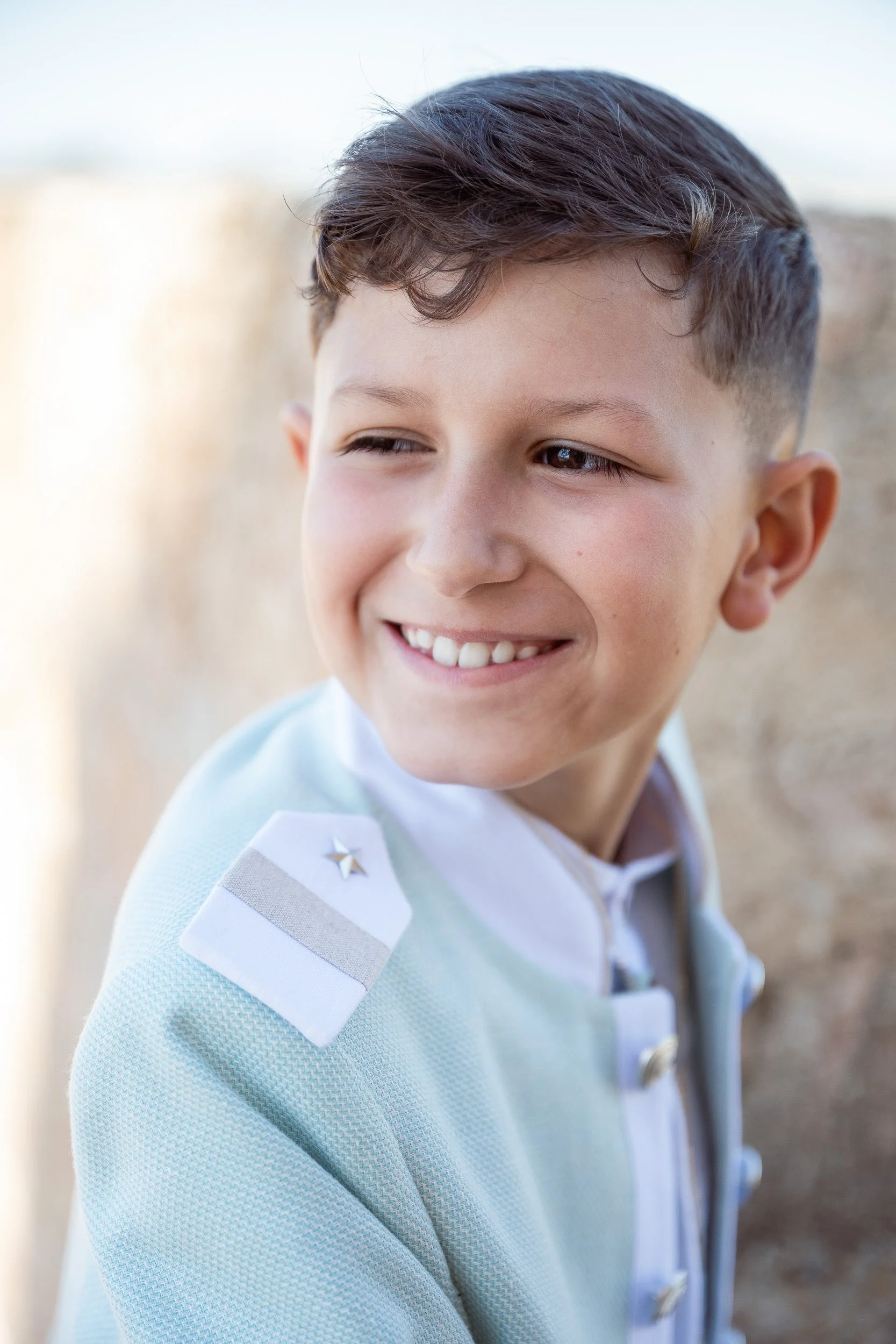 Retrato de un niño sonriente con ropa de comunión, en un fondo difuso y luz natural.