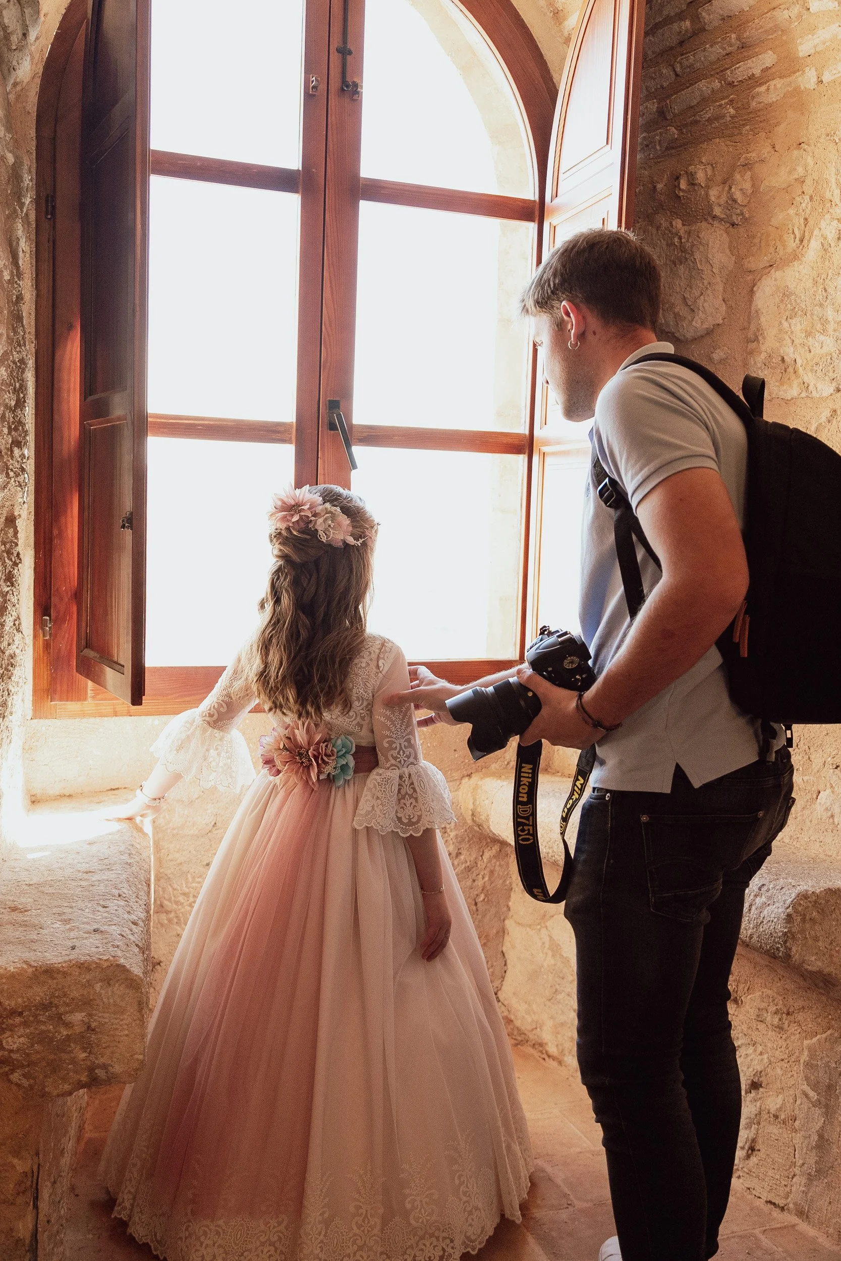 Una niña con un vestido largo de comunión es guiada por un fotógrafo en un castillo de Jumilla.