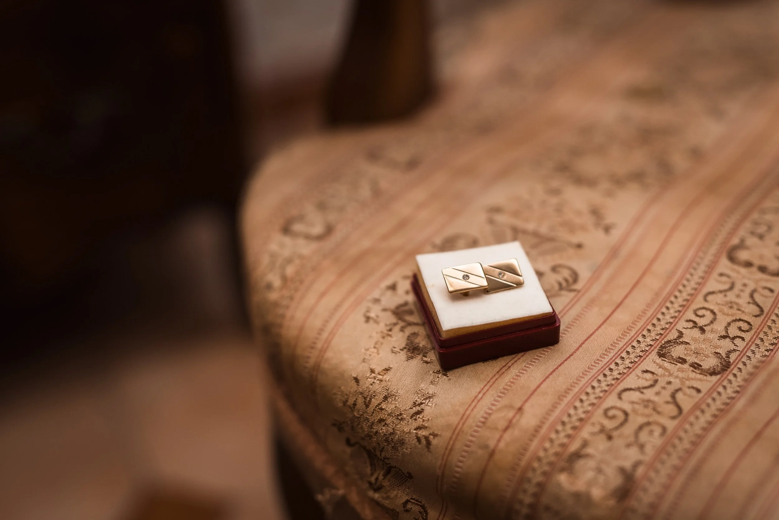 Anillo de oro con un diamante en una caja sobre tapiz decorativo.