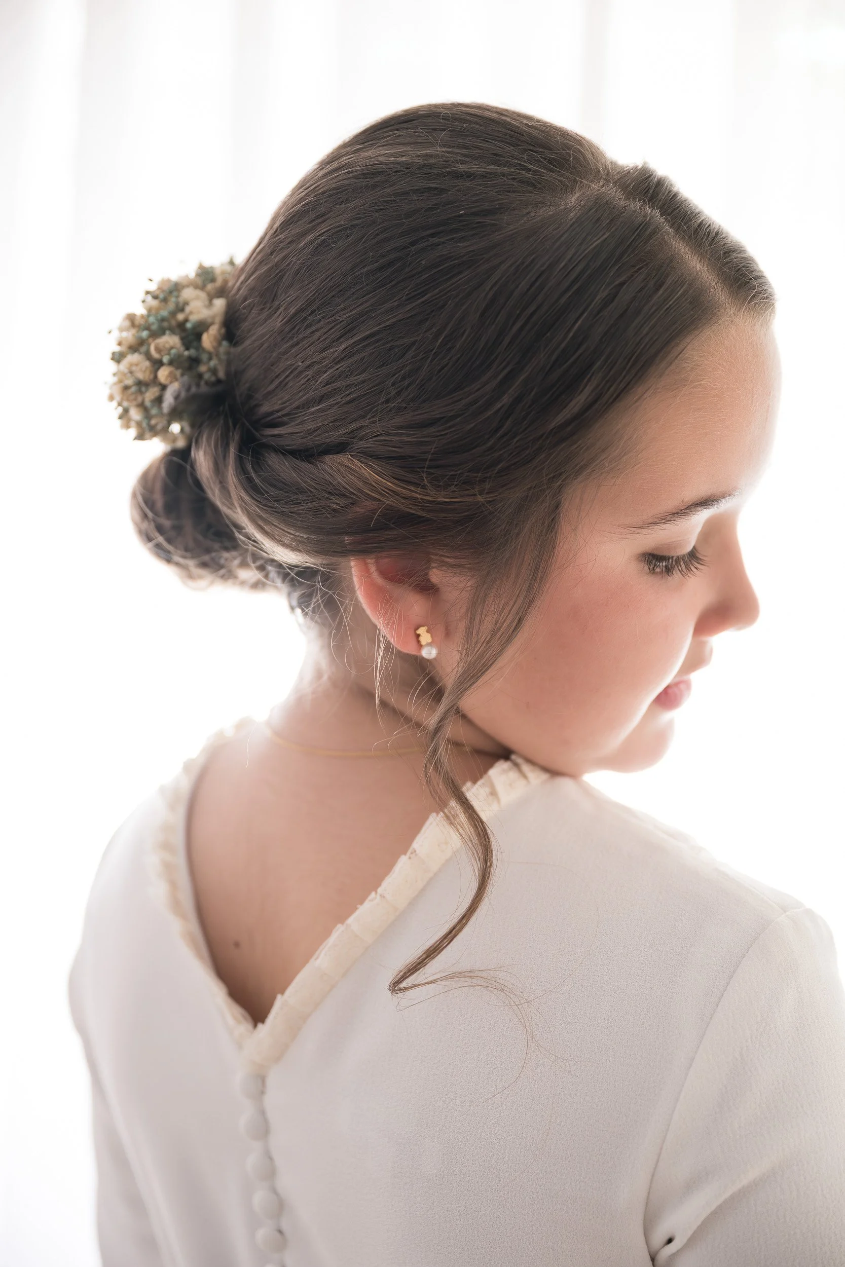 Mujer con cabello recogido y accesorios florales, vista lateral con fondo blanco