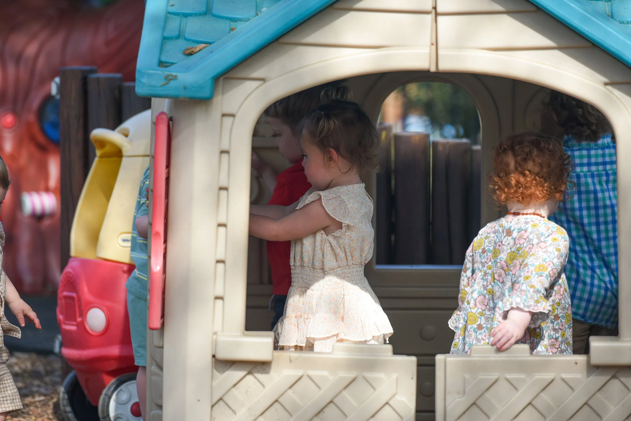 Children playing inside a plastic playhouse outdoors, with some children standing and others sitting inside.