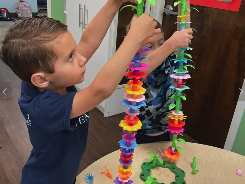Two children playing with colorful foam flower stacking toys in a classroom.