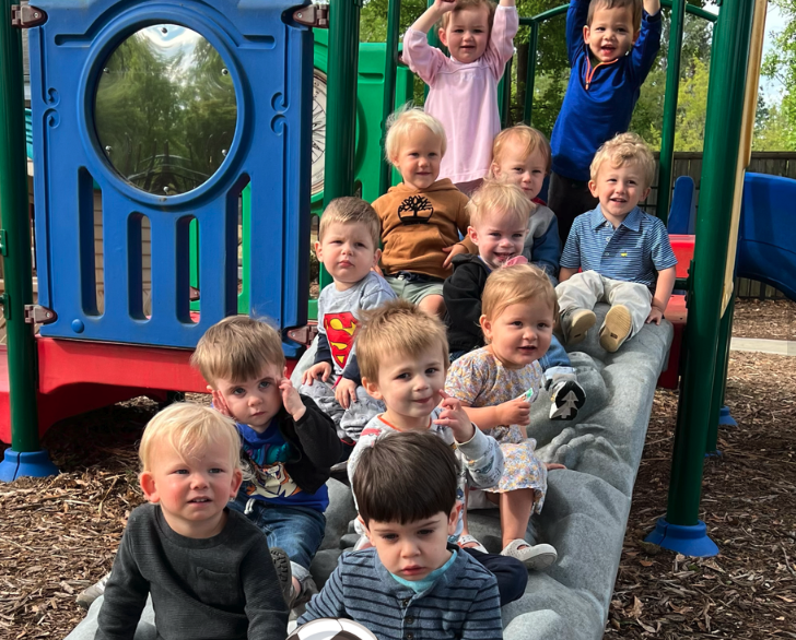 Group of young children sitting on a playground slide, smiling and playing outdoors.